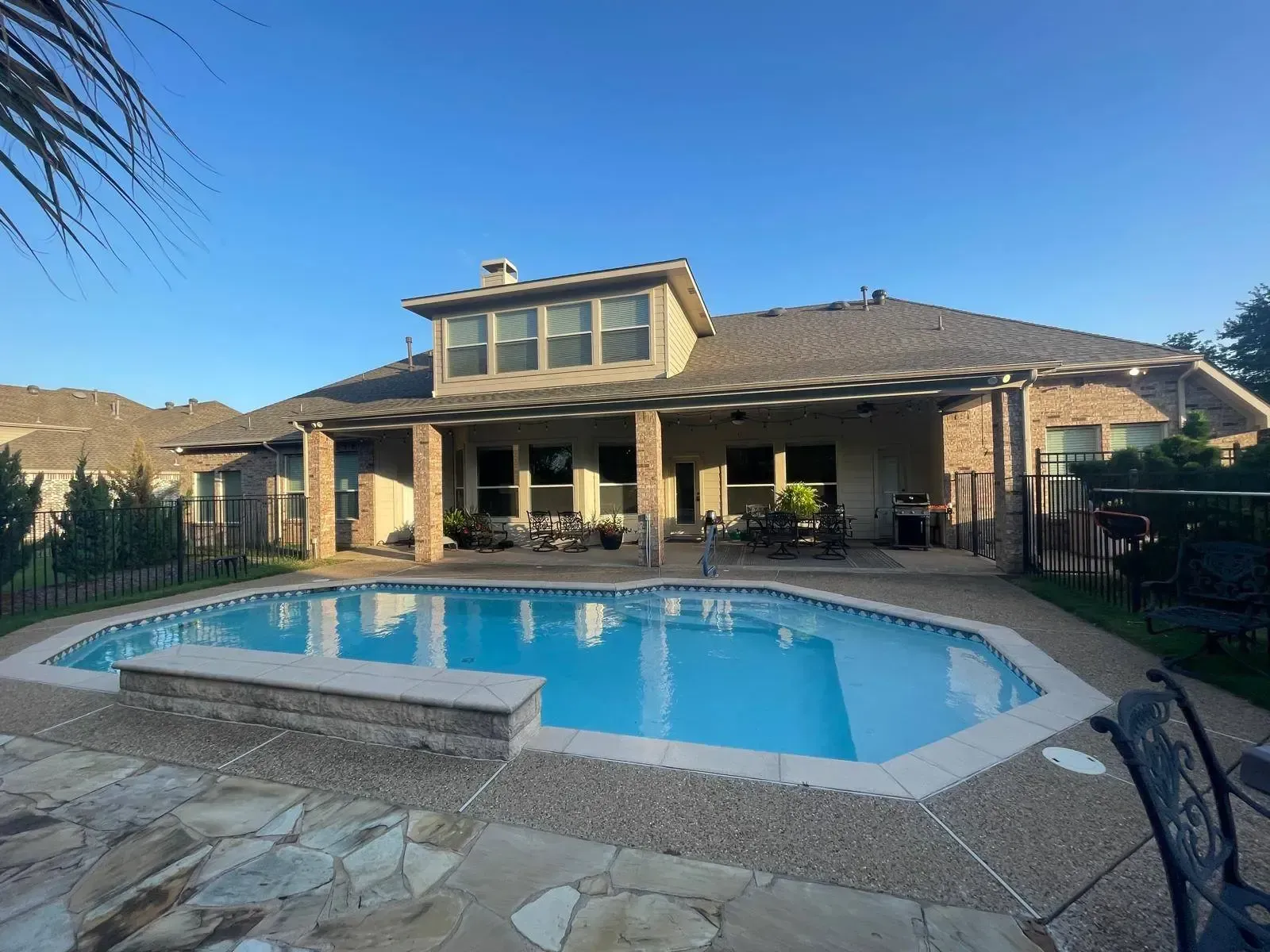 Backyard with pool, house, and patio under a clear blue sky.