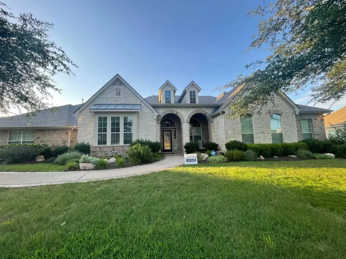 A single-story brick house with a green lawn and blue sky.