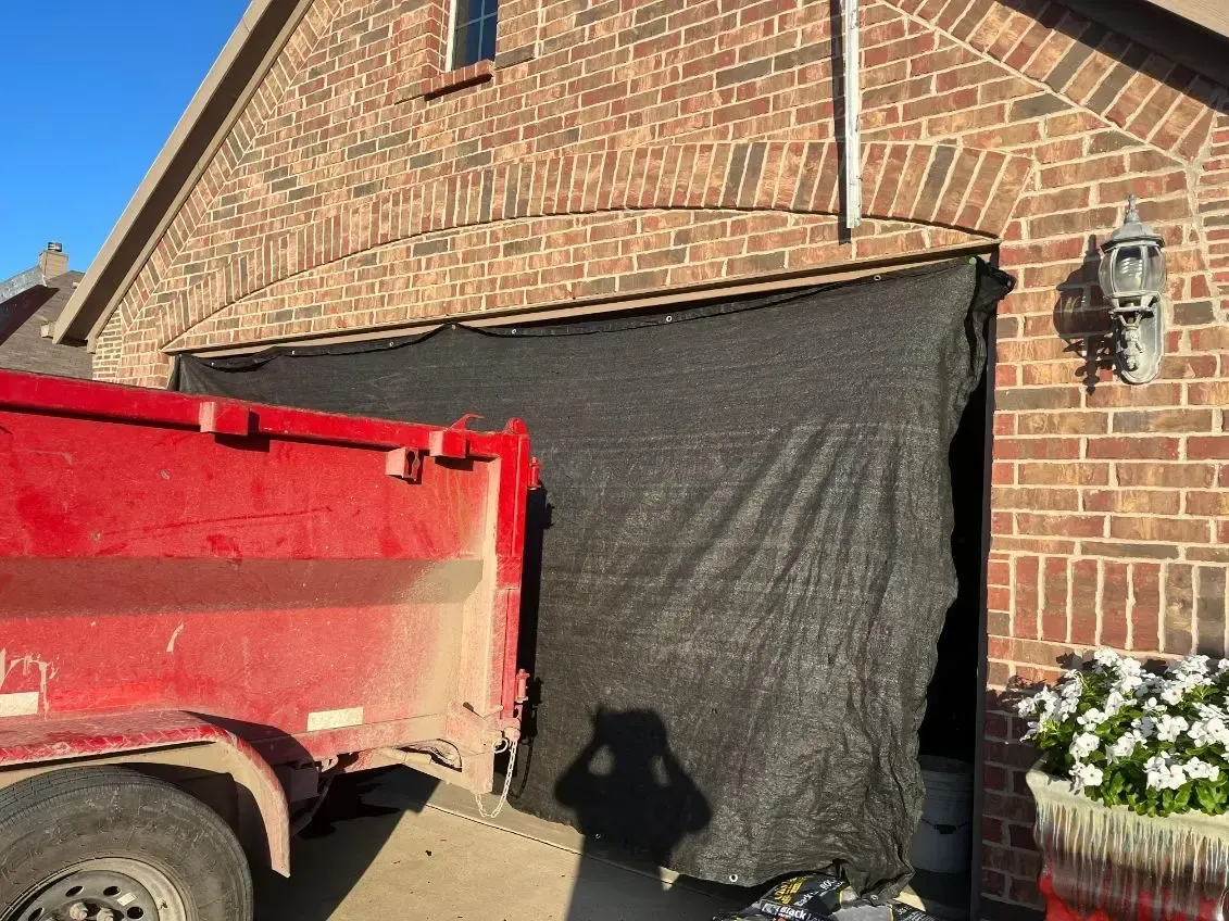 Red dump truck partially blocking a garage opening draped with black fabric; brick exterior.