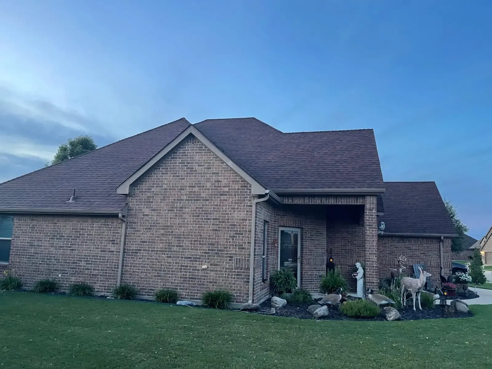 Brick house with brown roof and green lawn under a blue sky.
