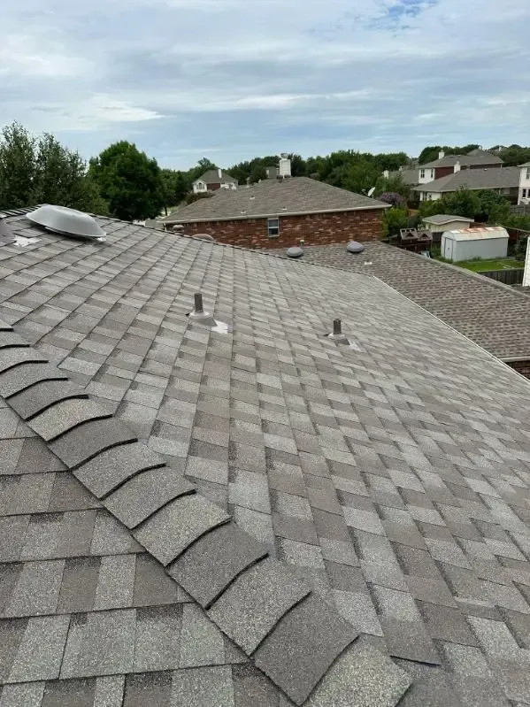 Gray asphalt shingle roof on a house, overcast sky, several vents and a skylight visible.