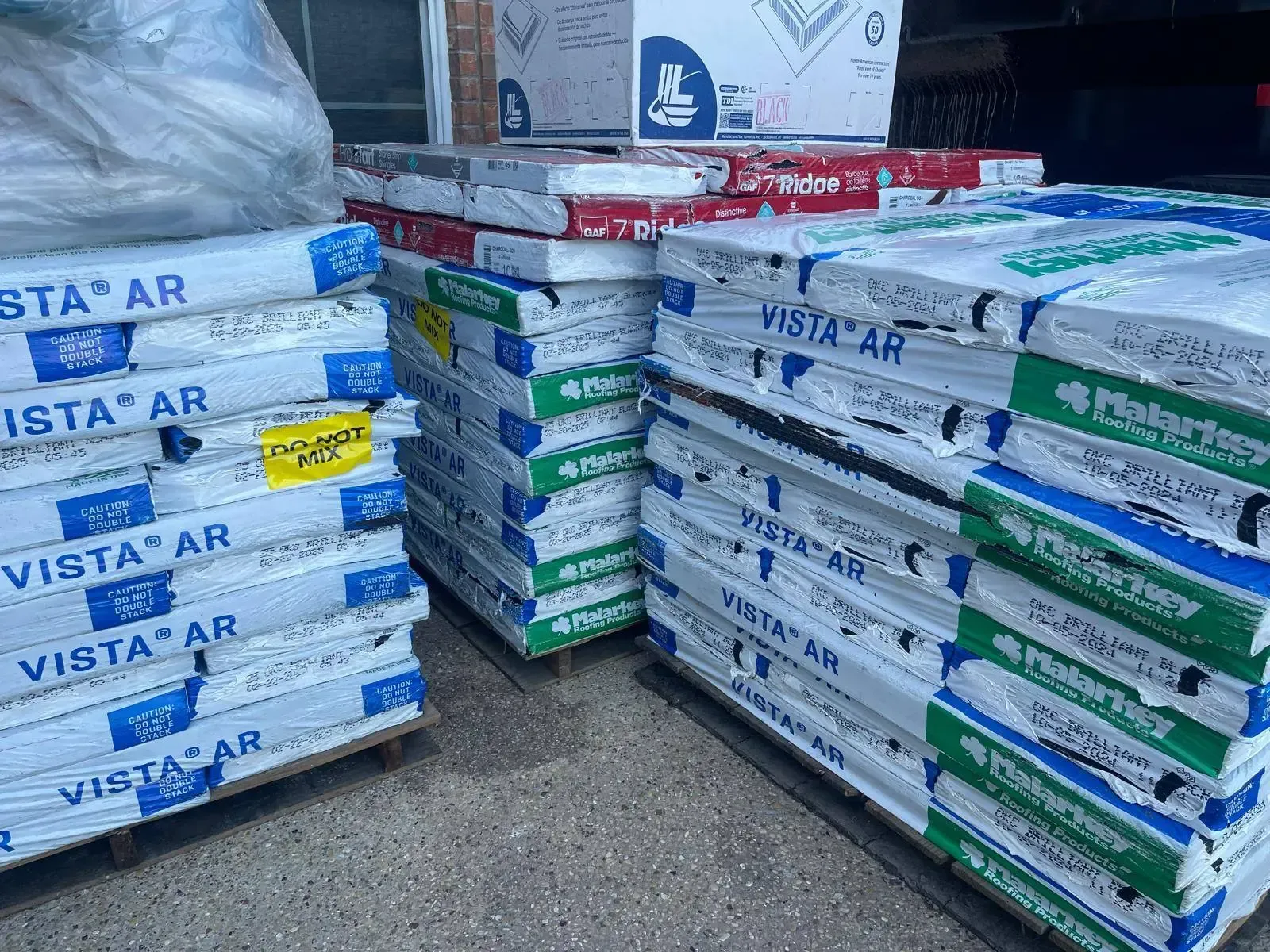 Pallets of packaged roofing materials stacked indoors, labels showing product names and colors.