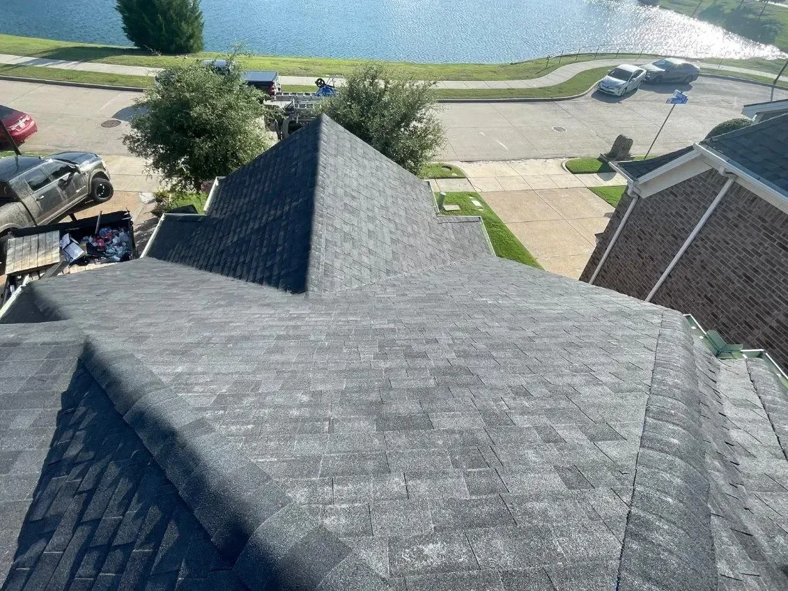 Overhead view of a house roof covered in gray shingles. A lake and neighborhood are in the background.