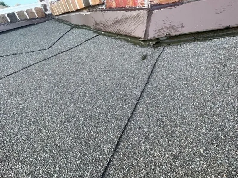 Close-up of a gray asphalt shingle roof, with a chimney and flashing visible.