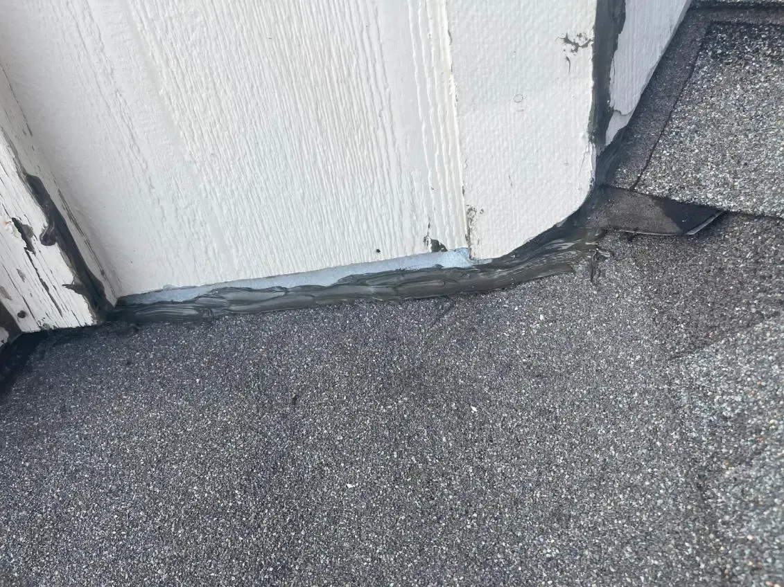 Close-up of roofing shingles next to white siding, sealed with gray sealant.