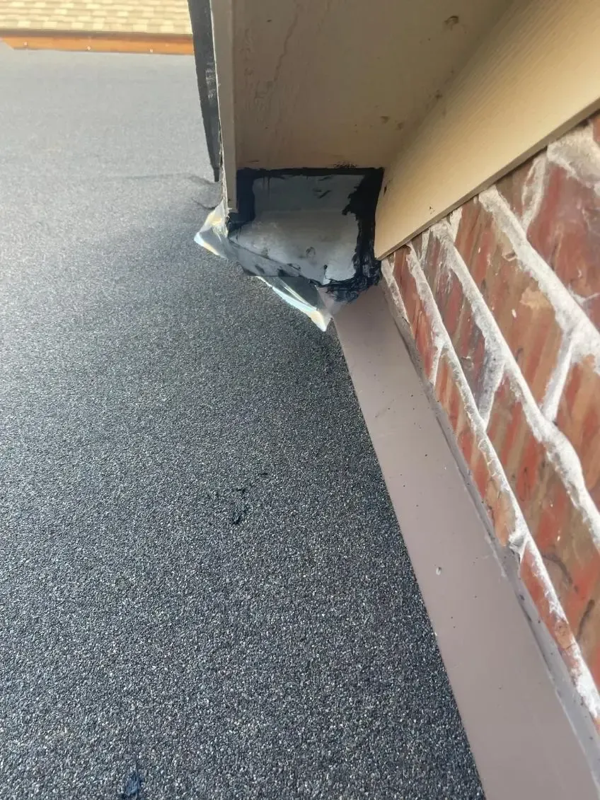 Close-up of a roof edge where a black flat roof meets a brick wall, sealed with white foam.