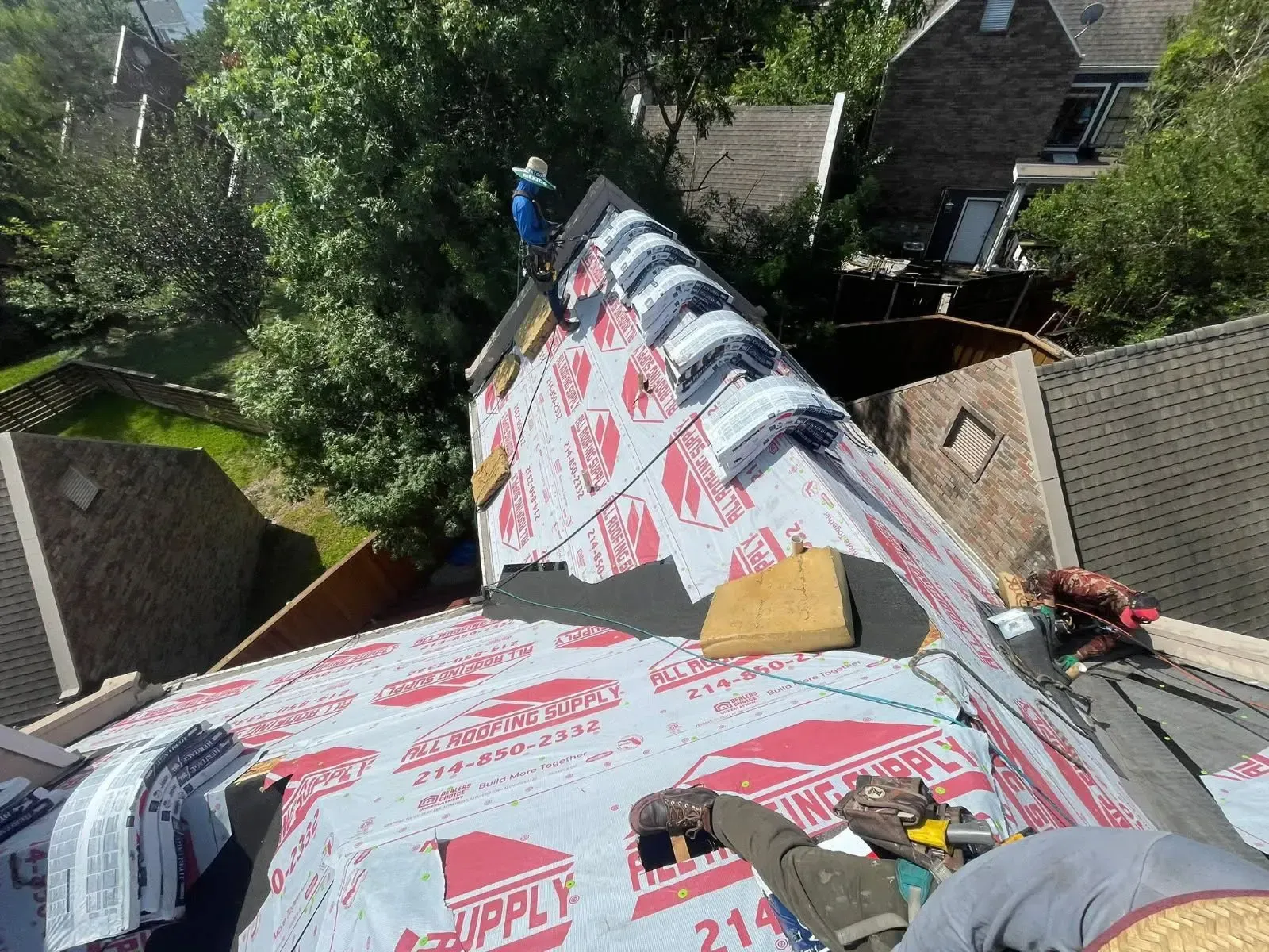 Roofers working on a residential roof, installing shingles and underlayment on a sunny day.