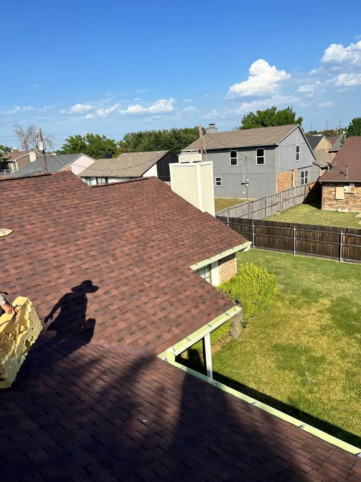 View of a residential neighborhood with rooftops and a green yard under a blue sky.