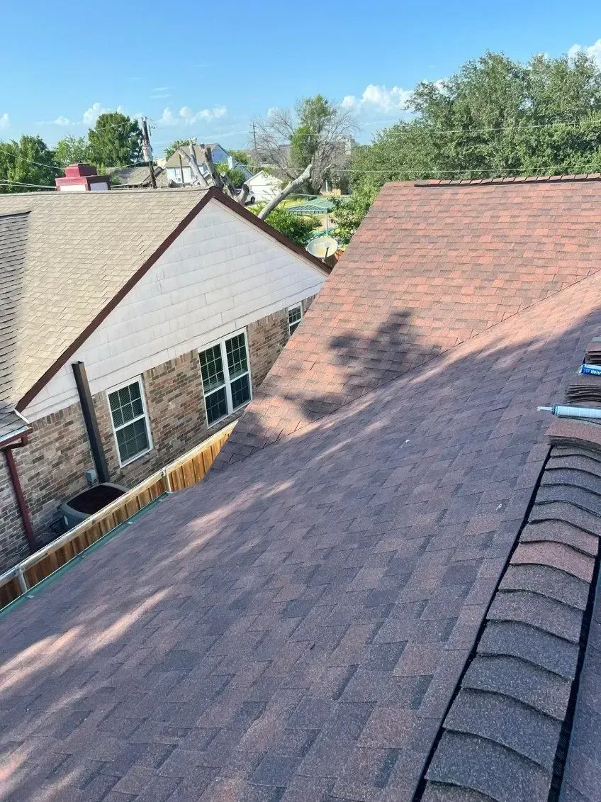 Rooftop view of houses with brown shingles, blue sky, and green trees.