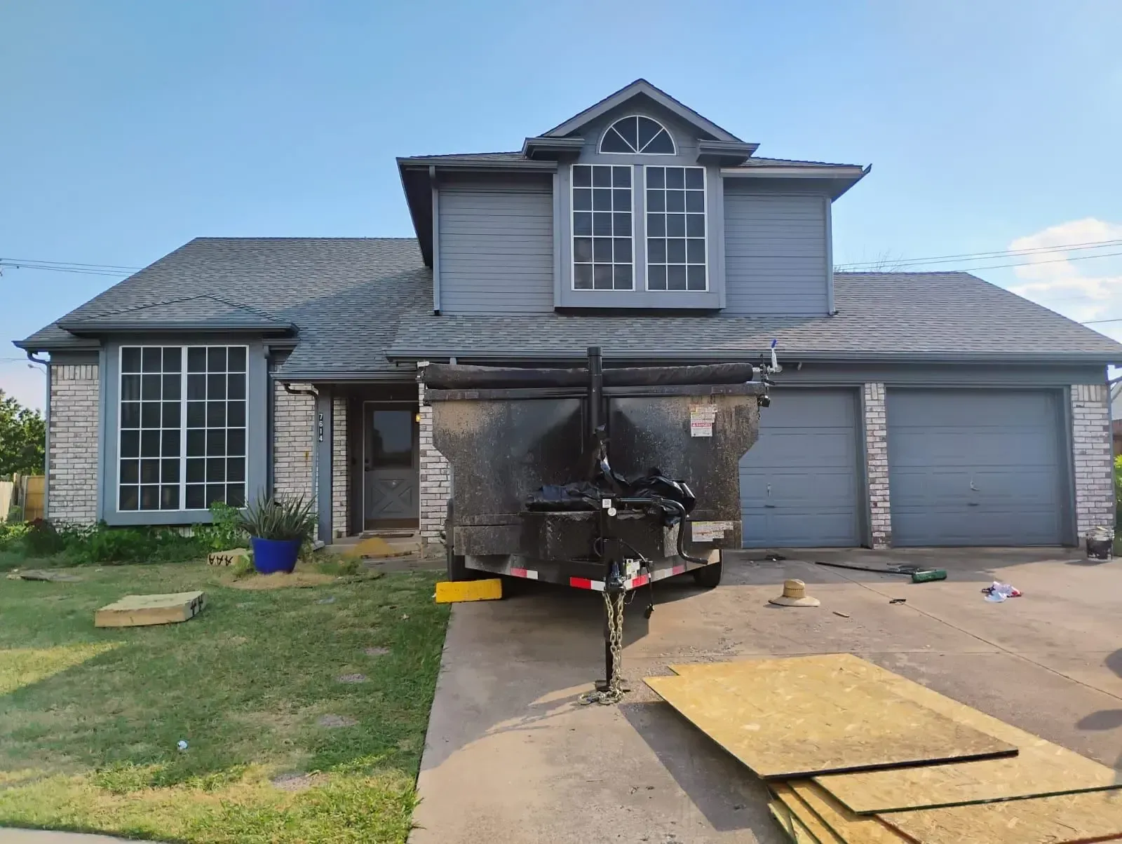 Two-story house with a dumpster in the driveway; roof repair in progress.