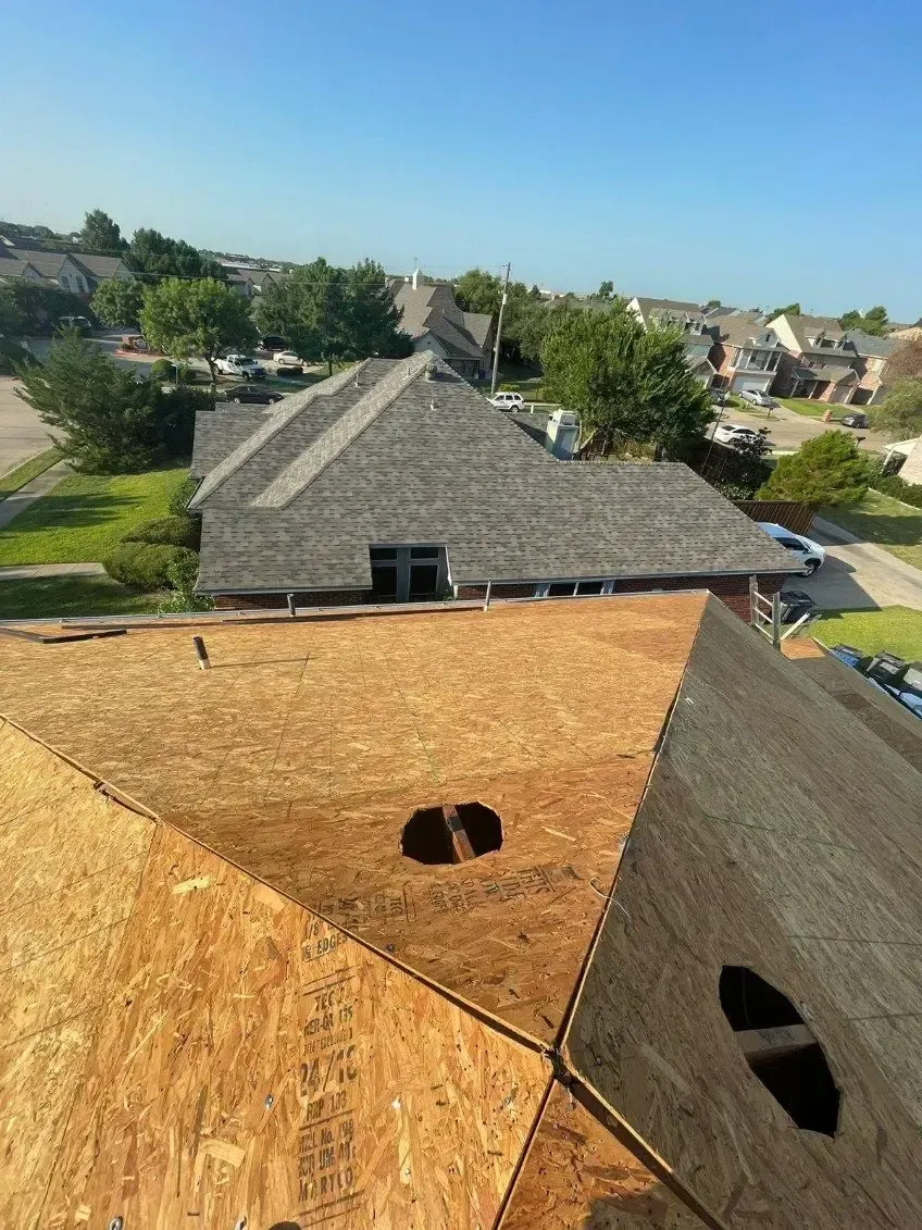 Construction in progress on a roof with visible wood and partially covered sections; residential area visible in background.