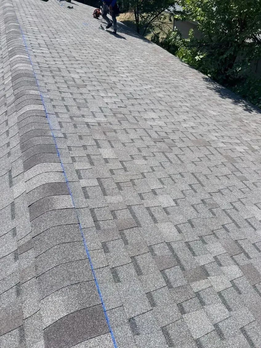 Person on a gray shingle roof, possibly working. Blue line visible along roof.