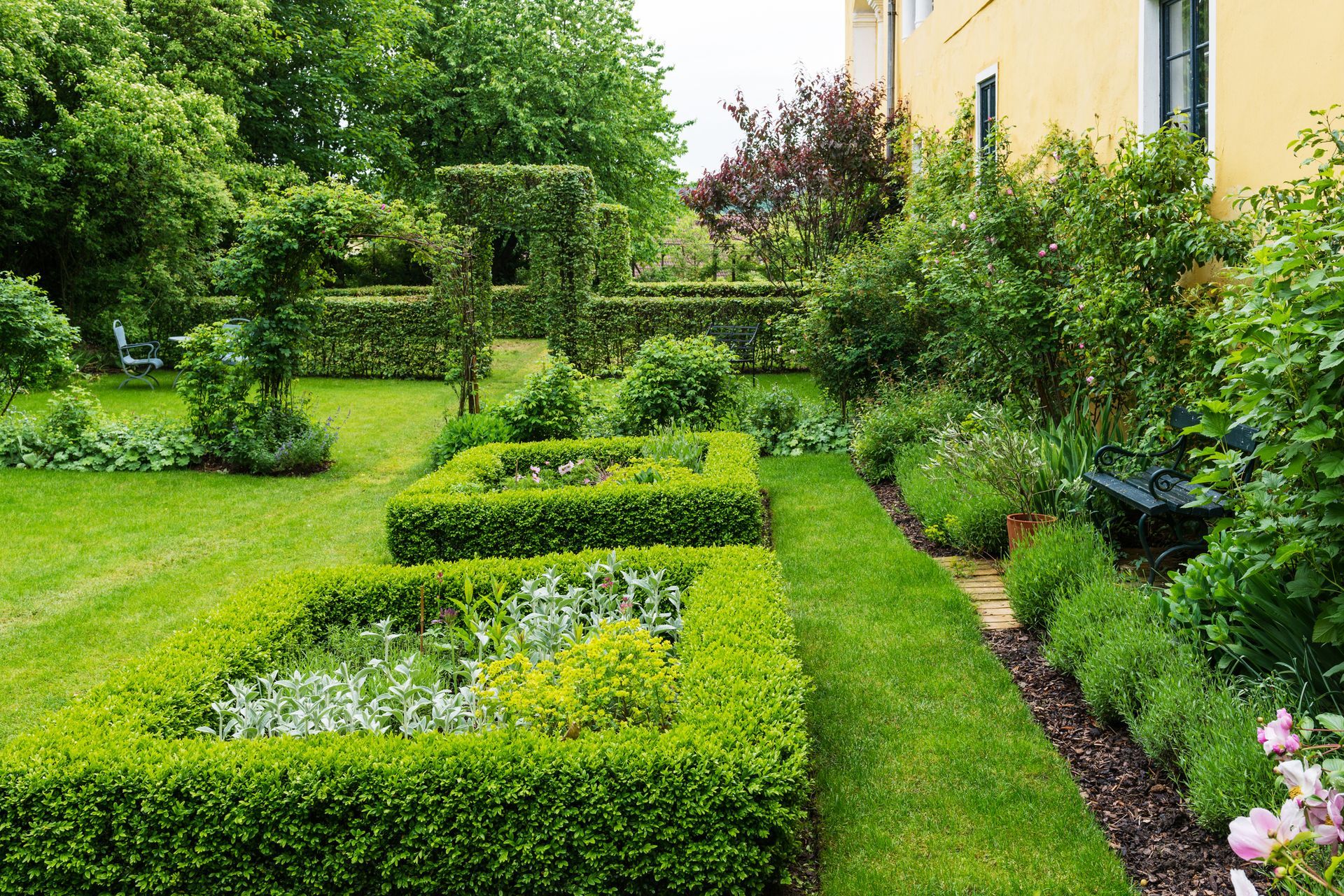 A lush green garden with a yellow building in the background