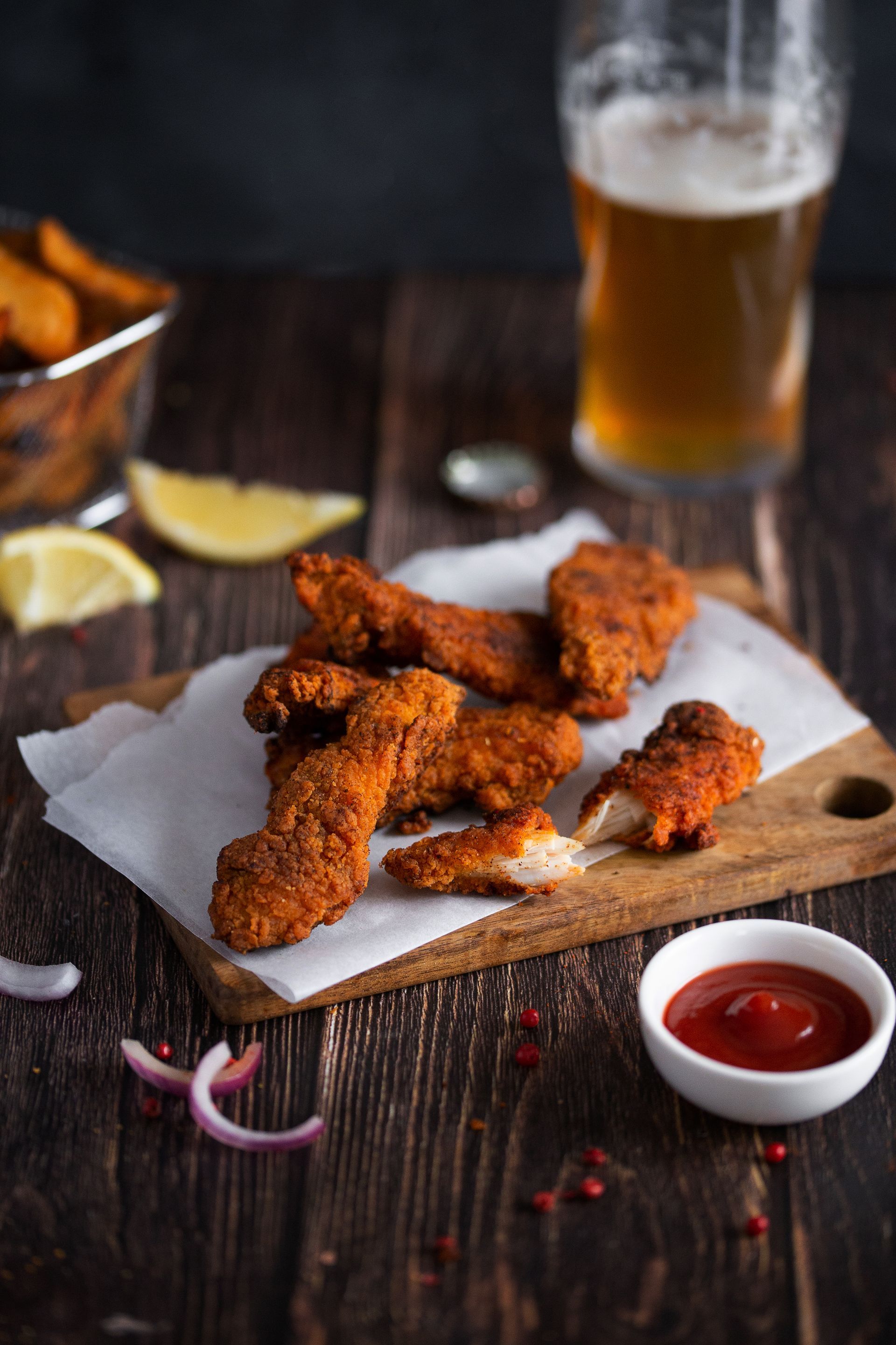 Ailes de poulet frites sur une planche à découper à côté d'un verre de bière.