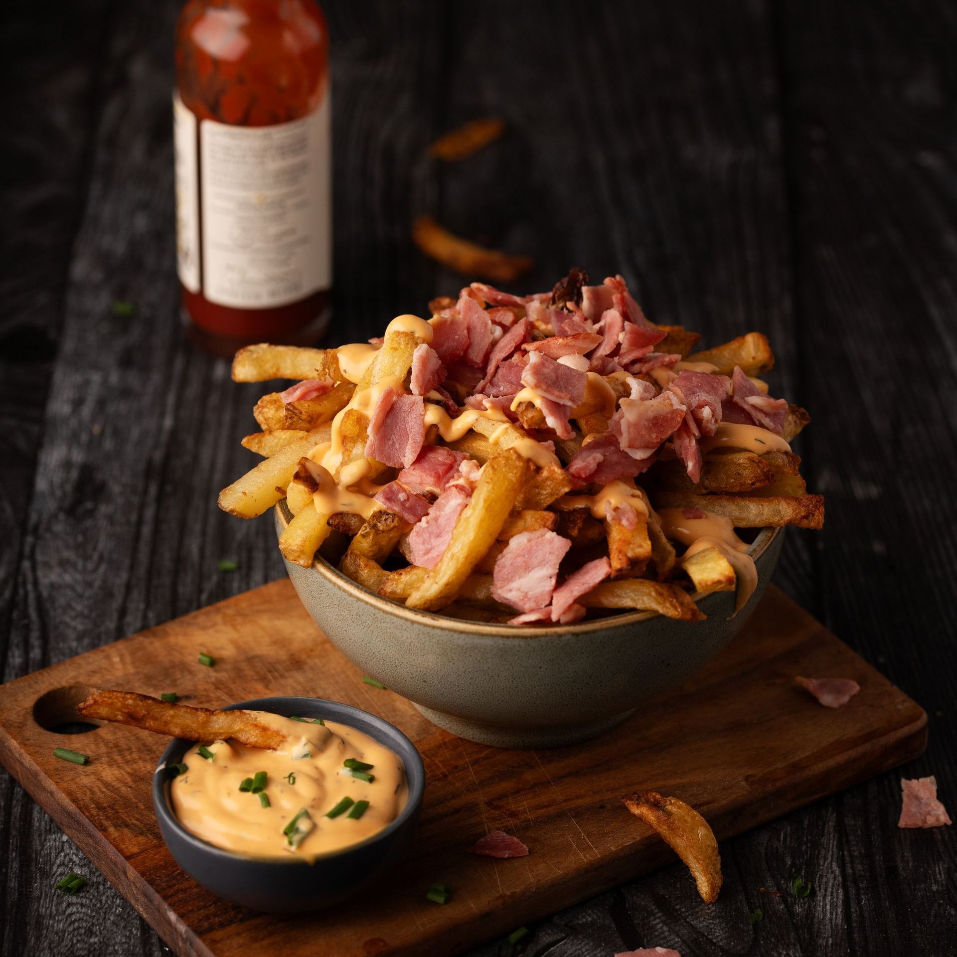 Un bol de frites avec du bacon et du fromage à côté d'un bol de sauce à trempette.
