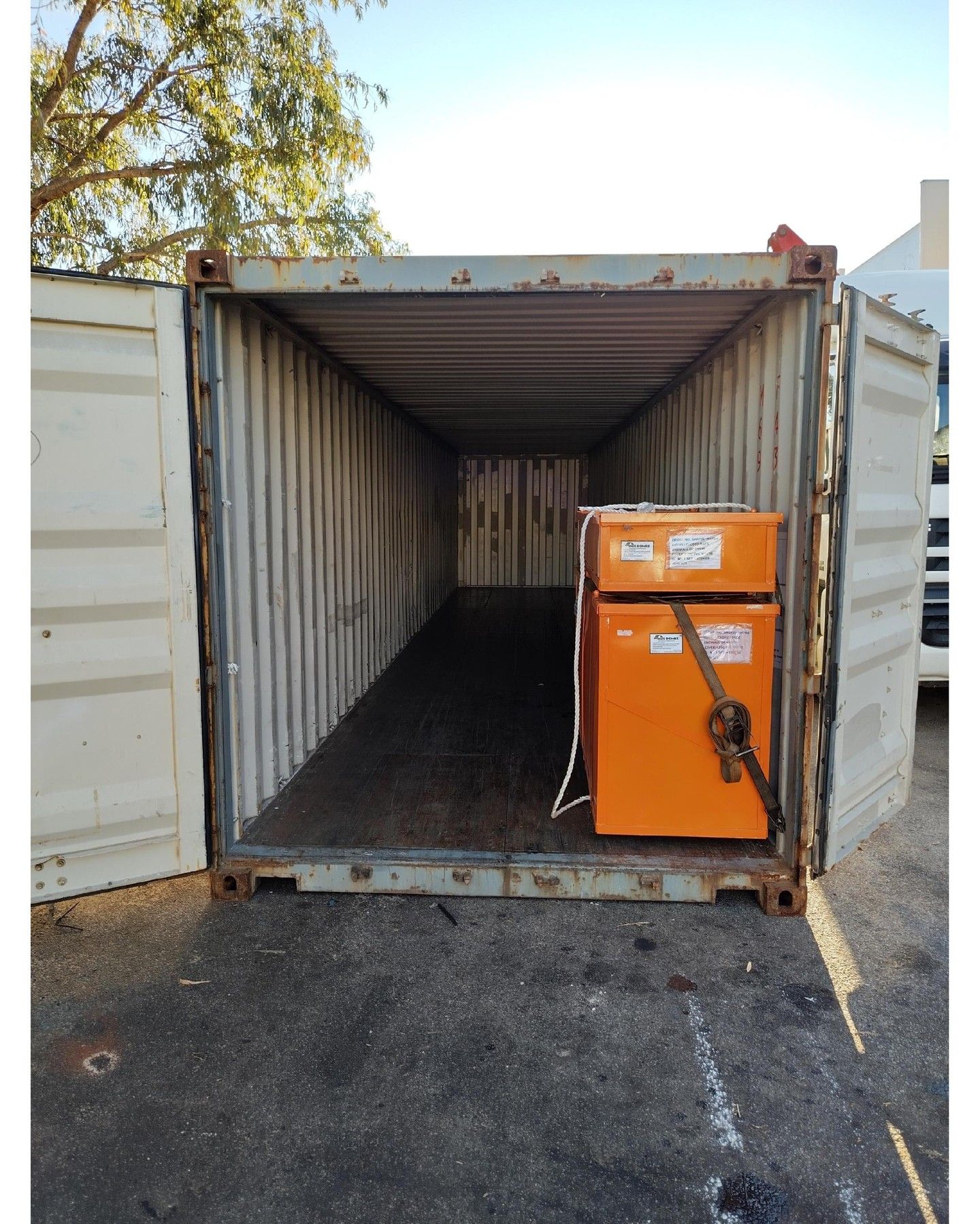 An orange box secured with straps inside an open shipping container on asphalt.