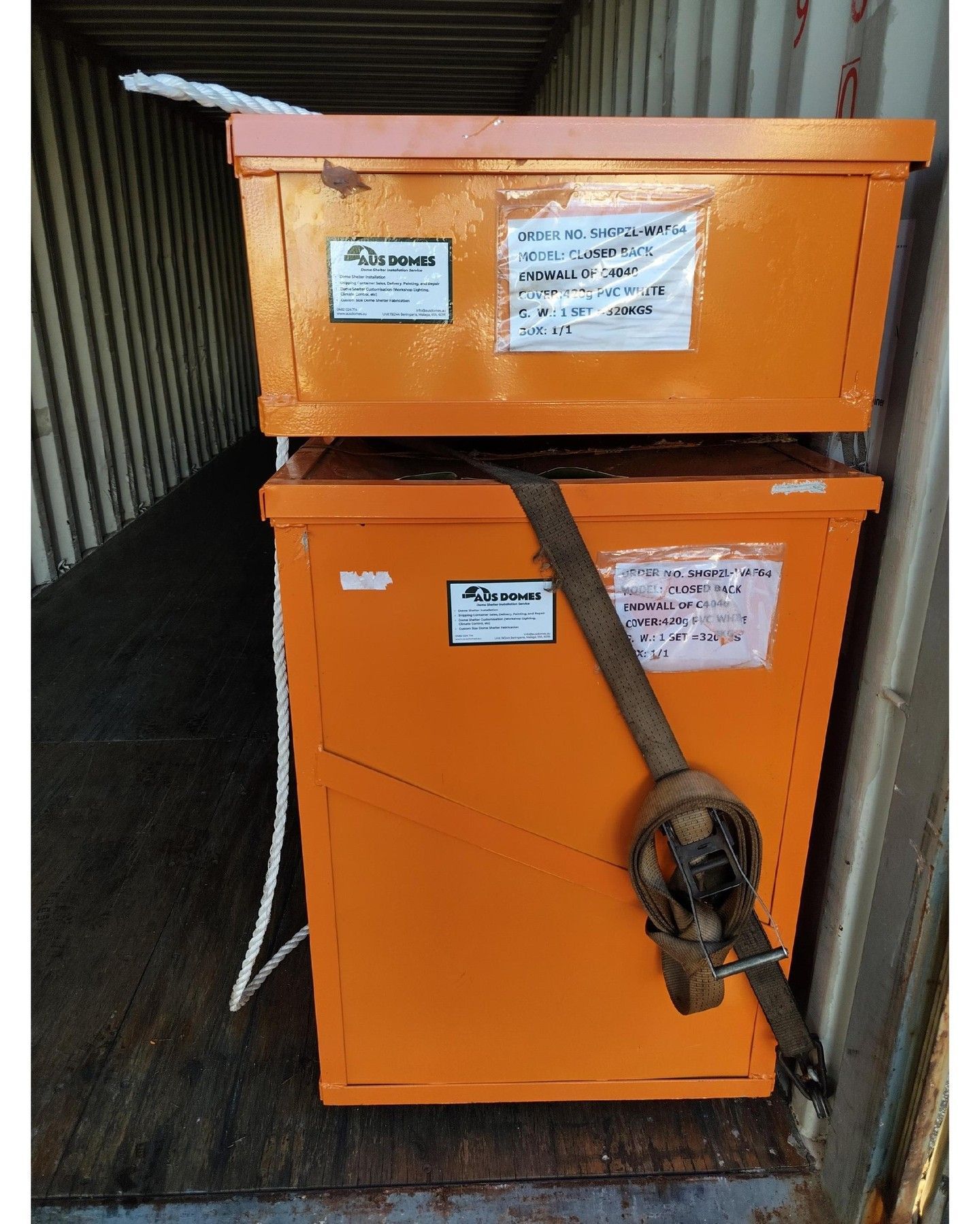 Two stacked orange metal boxes inside a shipping container, secured with a strap.