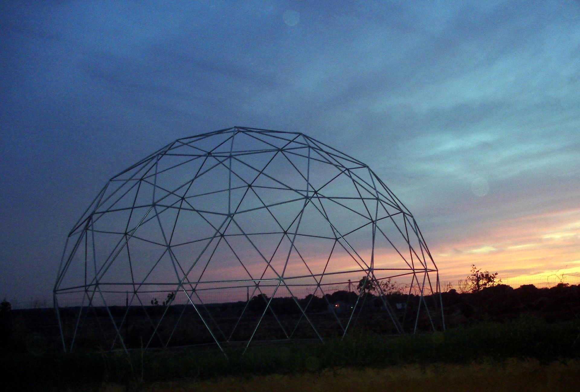 Steel geodesic dome frame against a sunset sky.