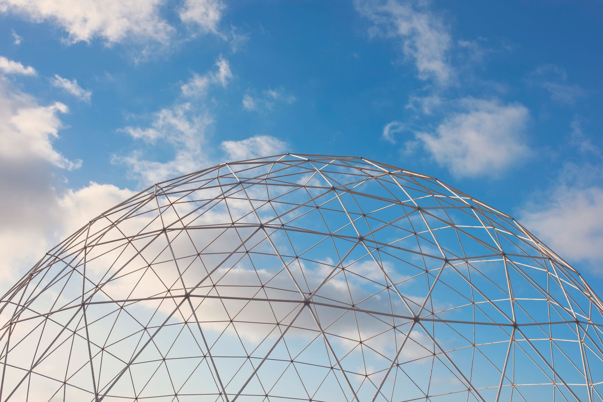 Geodesic dome frame against a blue sky with scattered clouds.