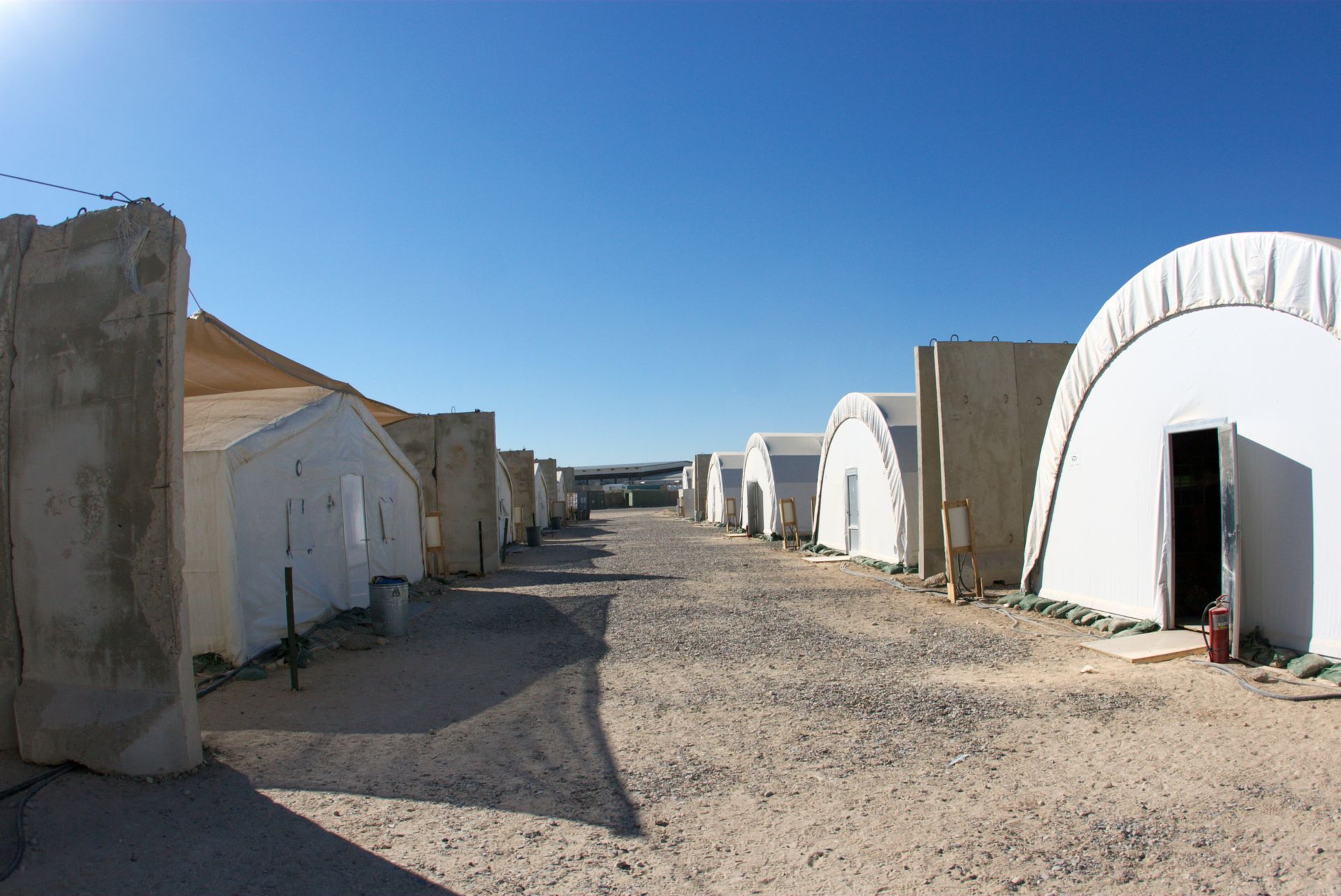 Row of white buildings with curved roofs, and concrete barriers, under a blue sky, in a desert setting.