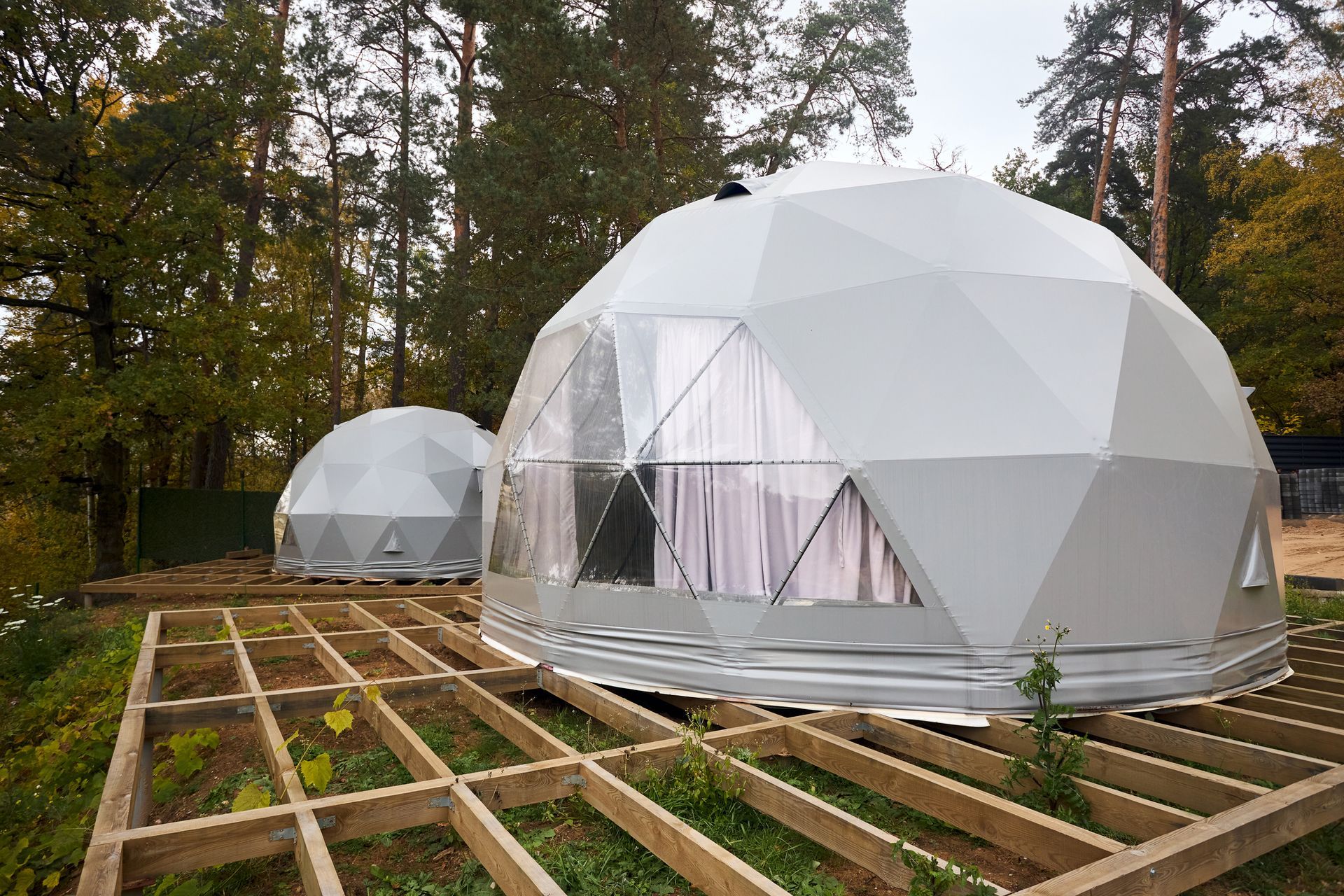 Two white geodesic dome structures on wooden platforms in a wooded area.