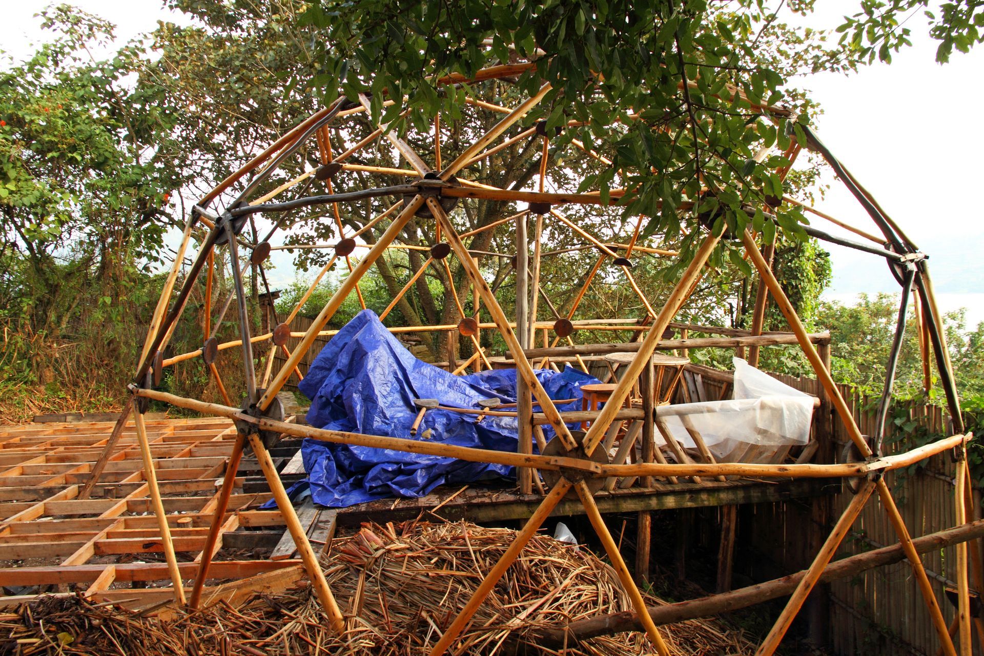 Bamboo dome structure under construction on a wooden platform; tarp covering interior.