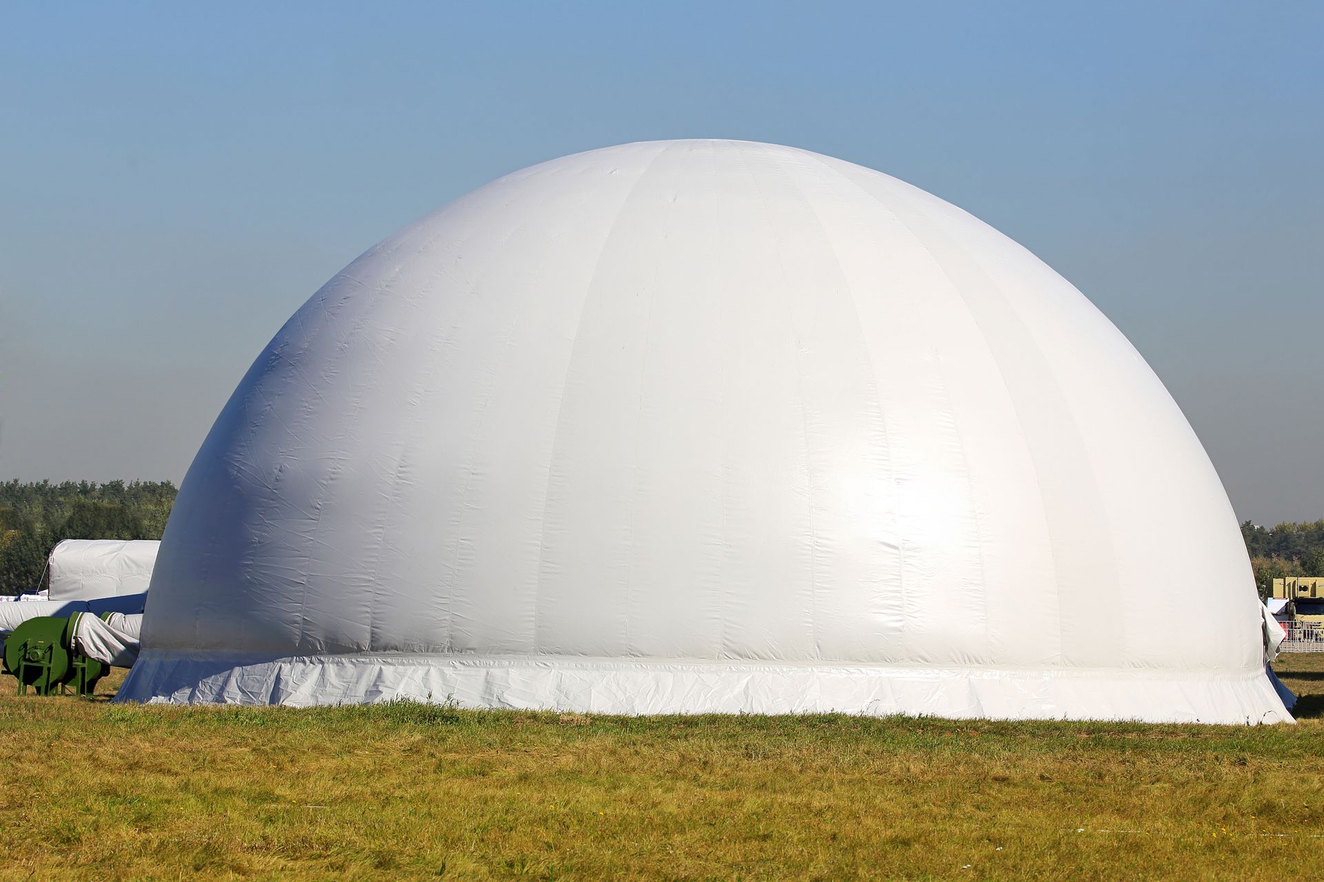 Large white dome structure on a grassy field under a clear blue sky.