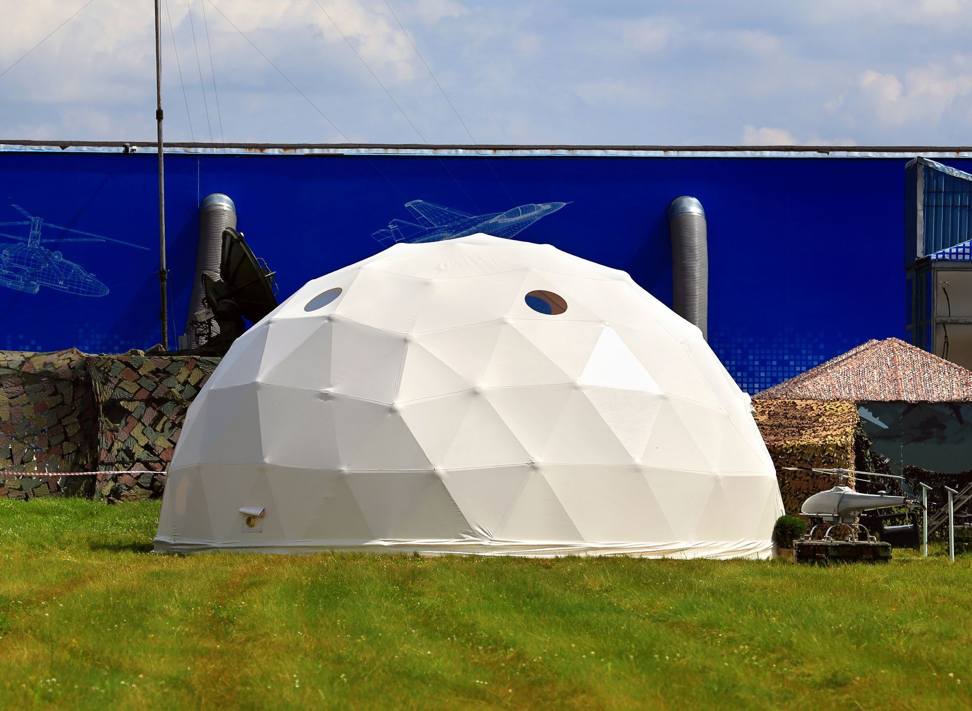 White geodesic dome structure on green grass, with blue backdrop and outdoor setting.