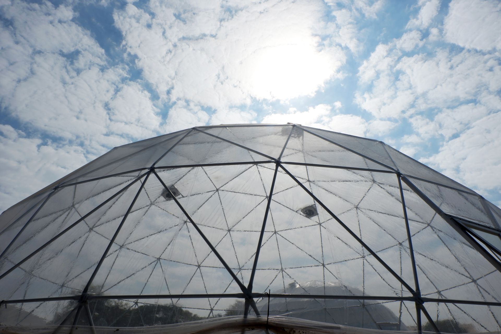 Geodesic dome against a blue sky with fluffy clouds and the sun shining brightly.