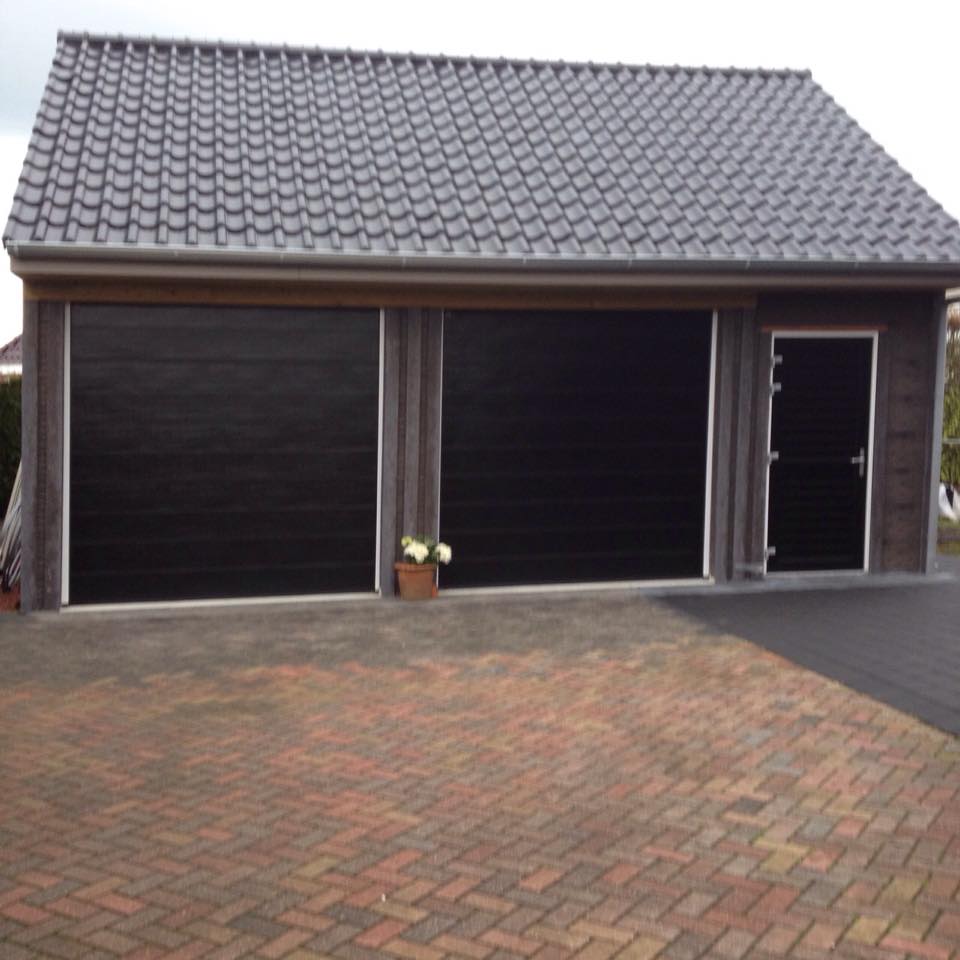 Dubbele houten garage met zwarte deuren en grijs pannendak, geplaatst op een oprit door A&B Betonbouw.
