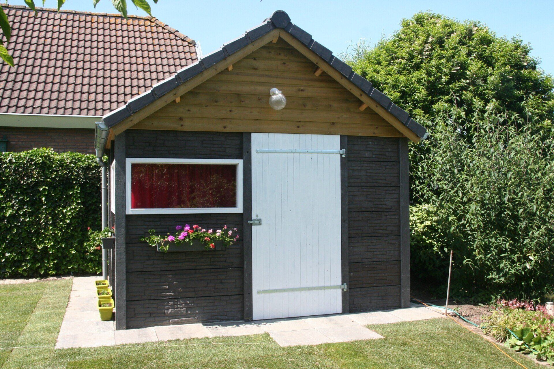 Kleine houten berging met wit deurpaneel en antraciet gevelbekleding, geleverd door A&B Betonbouw.