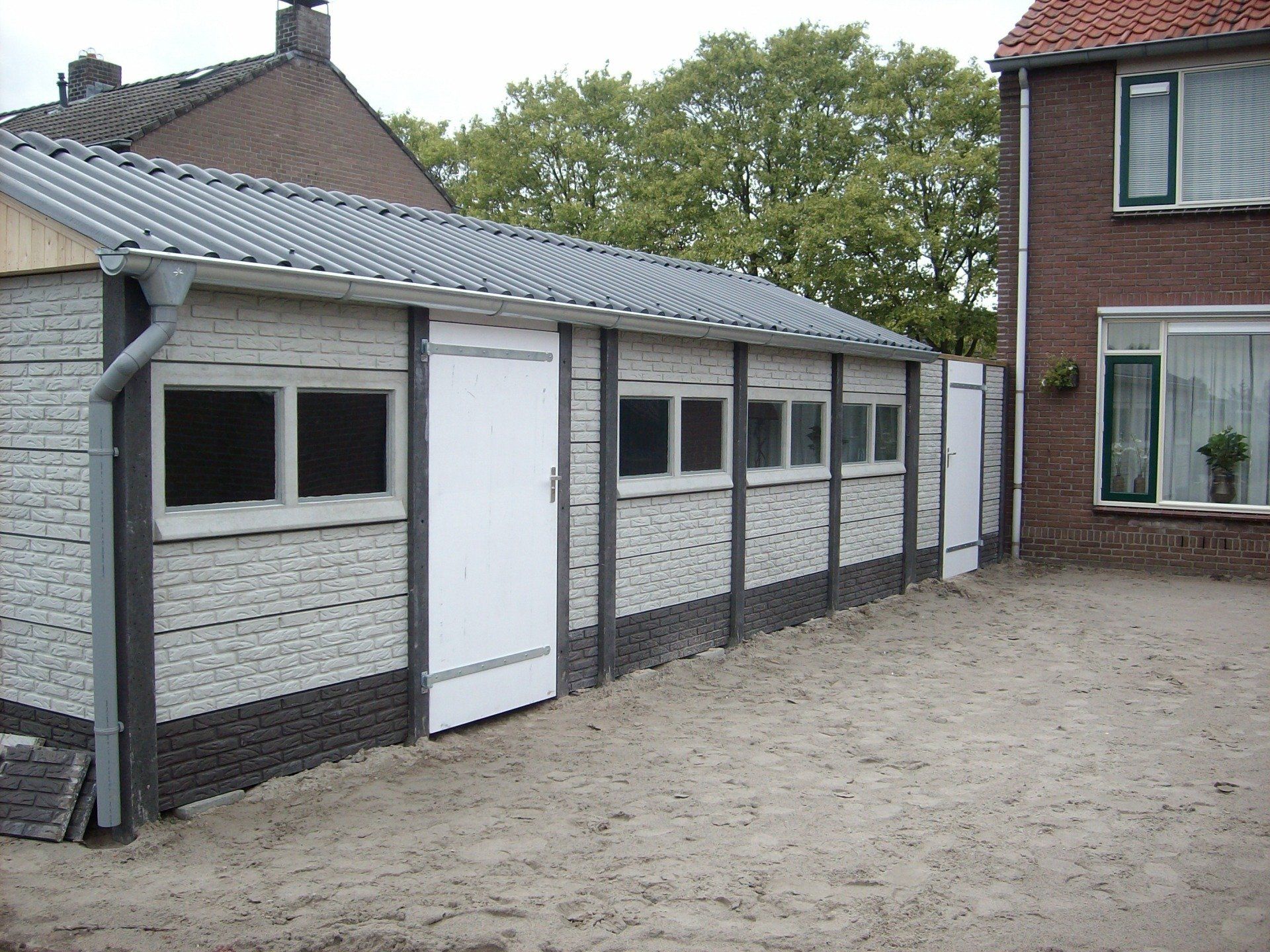 Betonnen garage met witte panelen en grijs dak, gebouwd naast een woning door A&B Betonbouw.