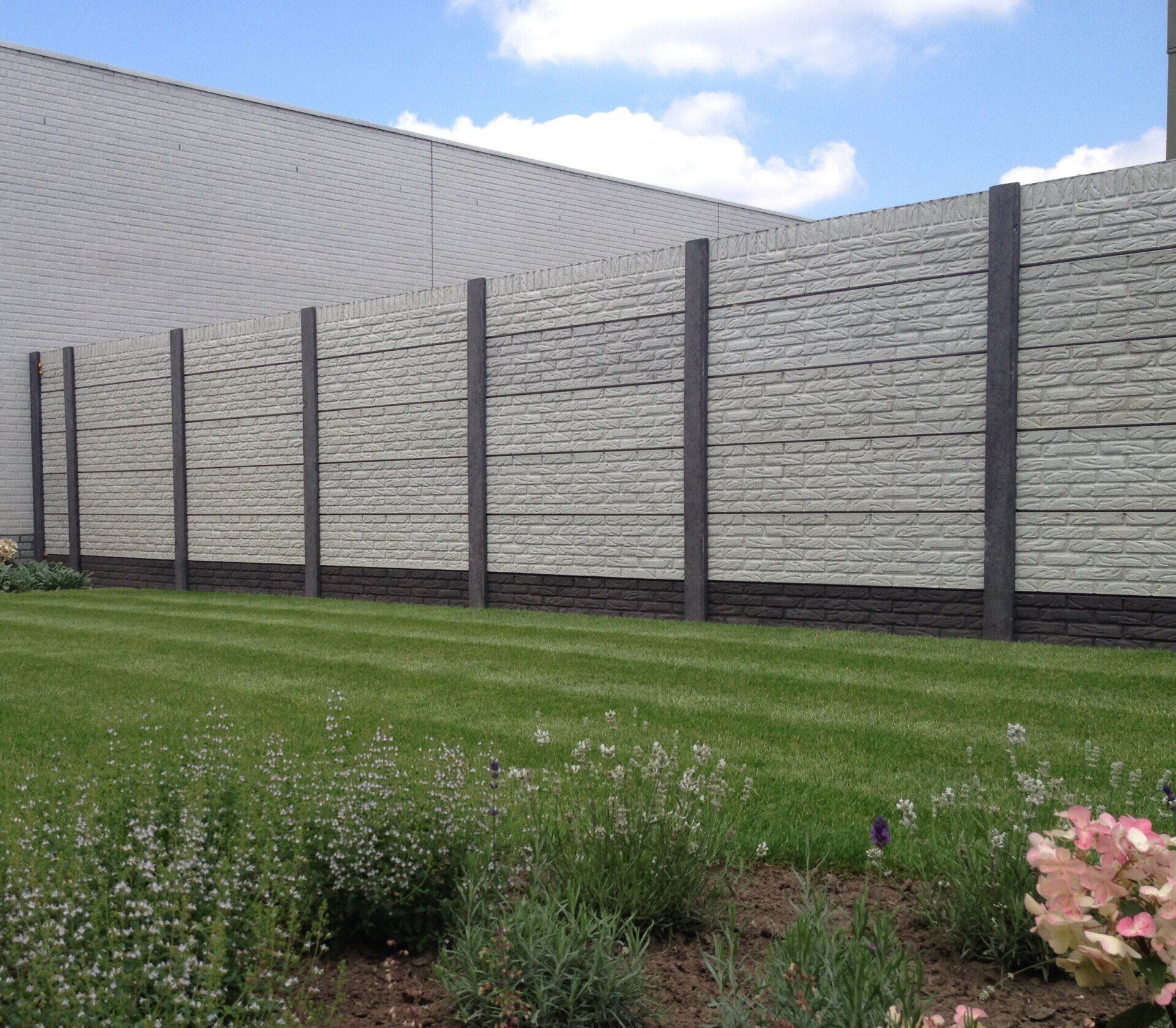 Lange betonnen schutting met grijze steenmotief panelen, geplaatst door A&B Betonbouw.