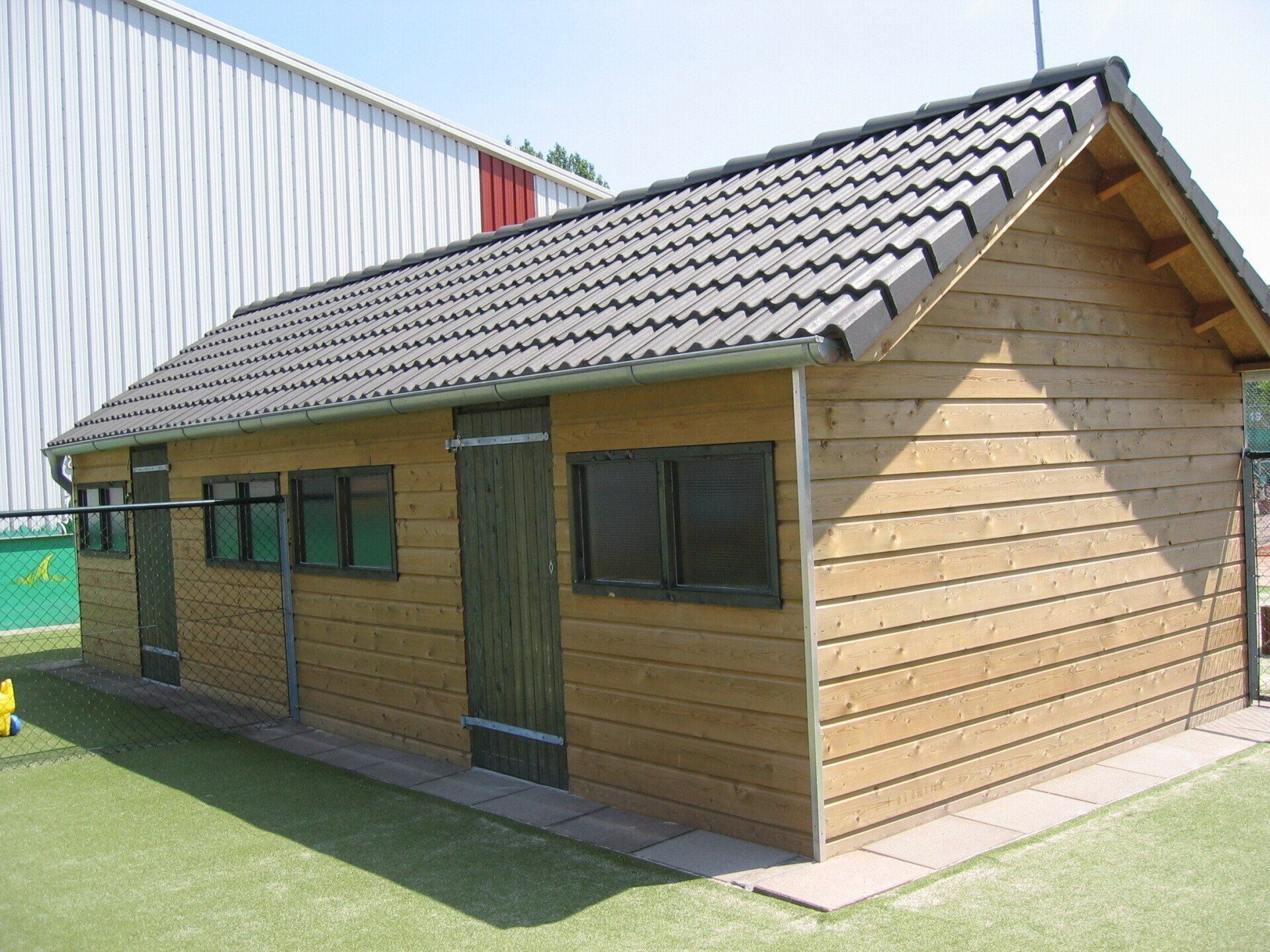 Houten berging met rood pannendak en ramen, geplaatst door A&B Betonbouw.