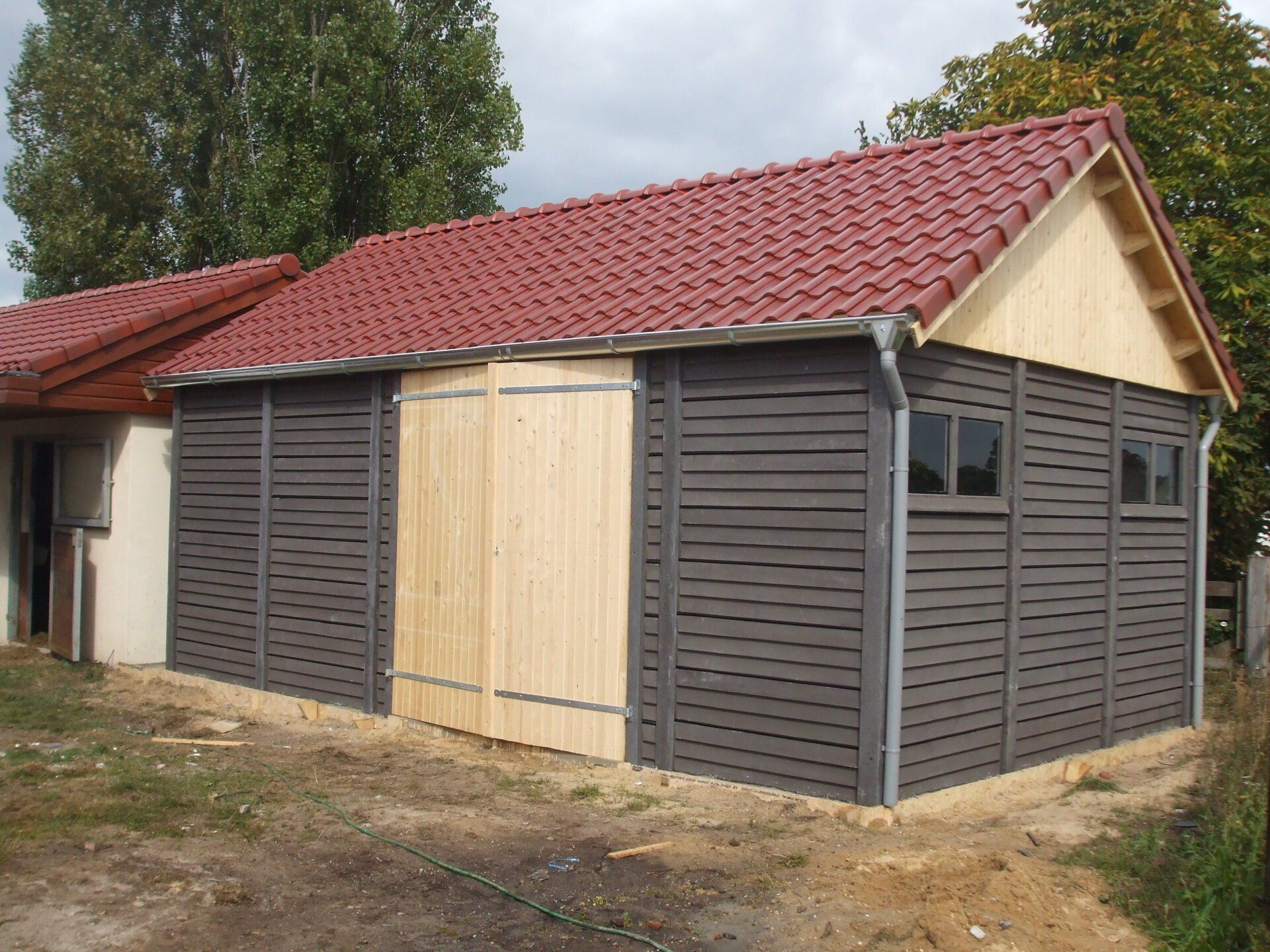 Houten loods met rood pannendak en betonnen onderbouw, maatwerkproject van A&B Betonbouw.