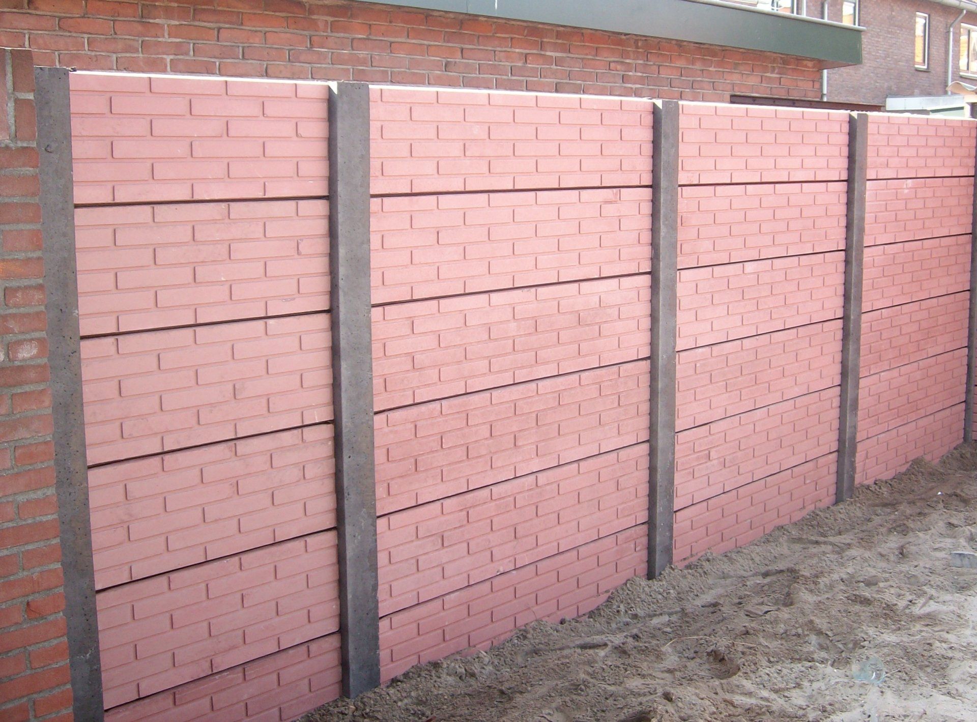 Rode betonschutting met steenmotief panelen en grijze palen, duurzaam project van A&B Betonbouw.