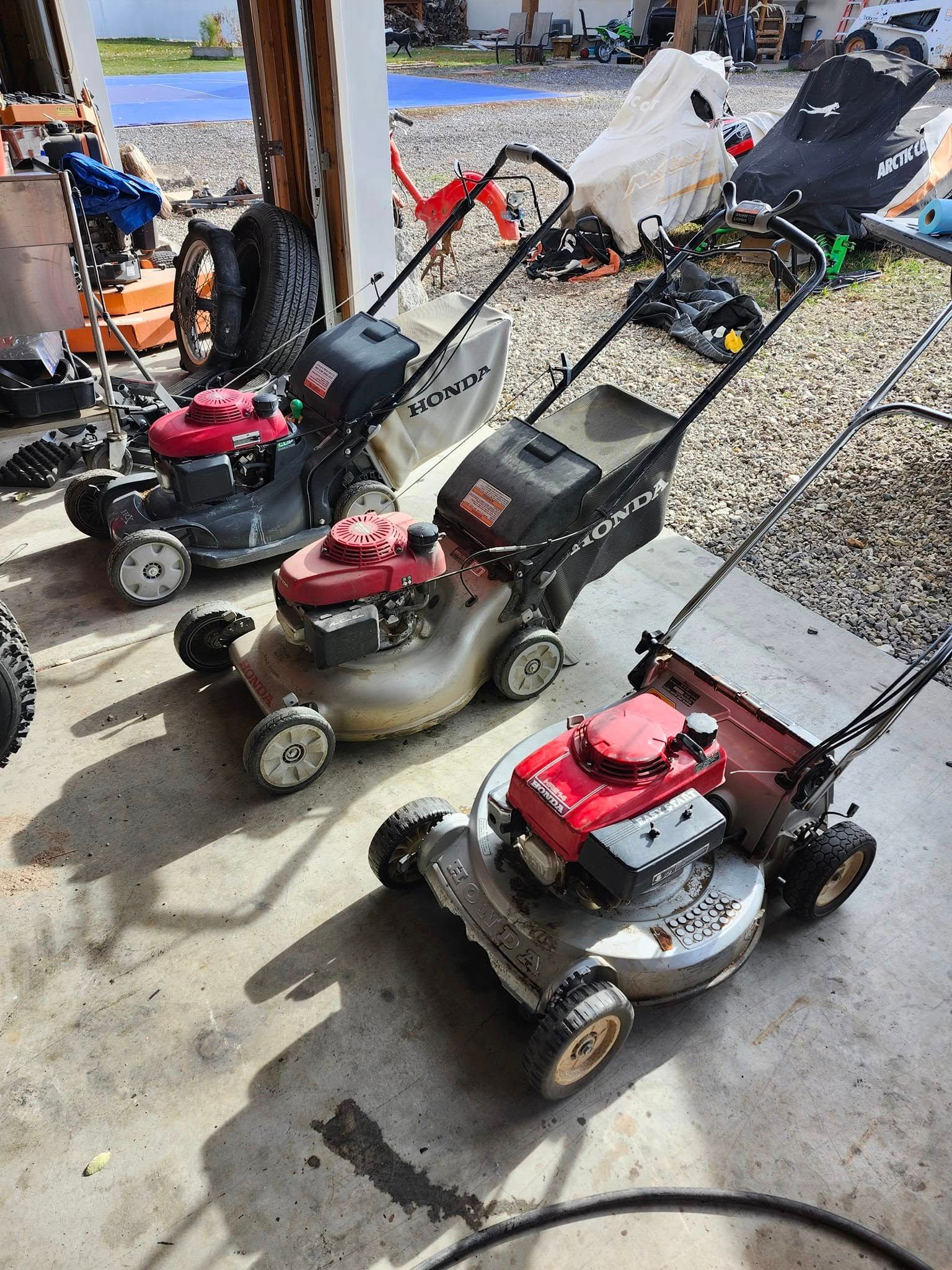 Three Honda lawnmowers with red engines and black and silver decks parked on a concrete surface.