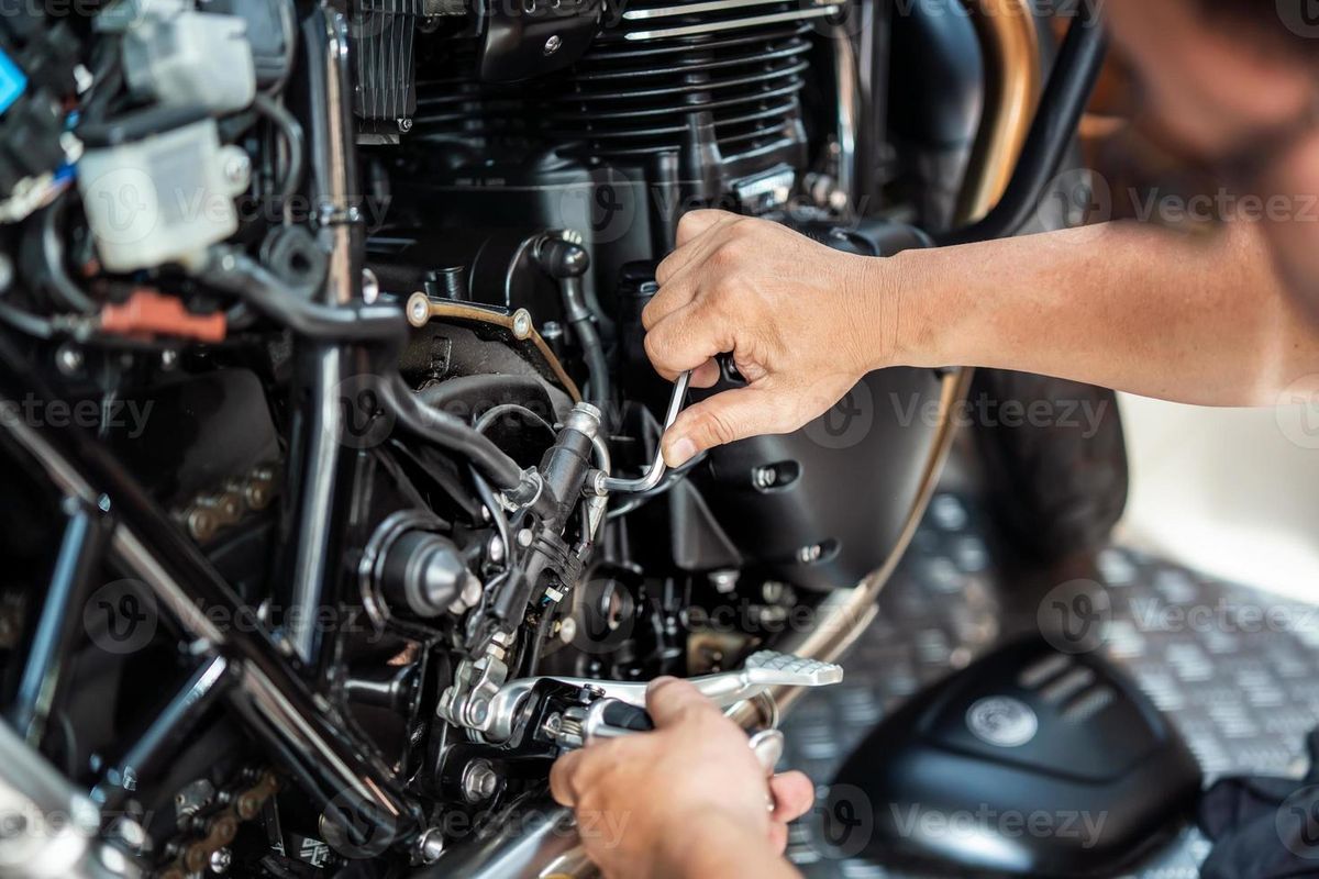Person working on a motorcycle engine with tools. Black engine and frame, close-up shot.