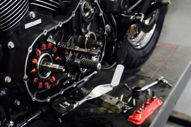 Motorcycle engine partially disassembled on a workbench. Black components with exposed internal parts and tools.