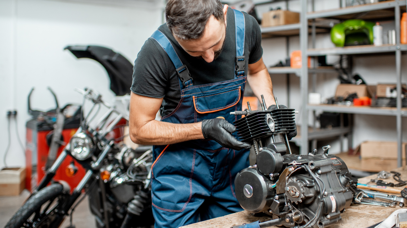 Mechanic in blue overalls working on a motorcycle engine in a garage.