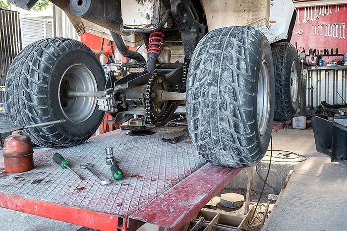 ATV raised on a lift in a repair shop, showing rear tires, tools, and mechanical components.