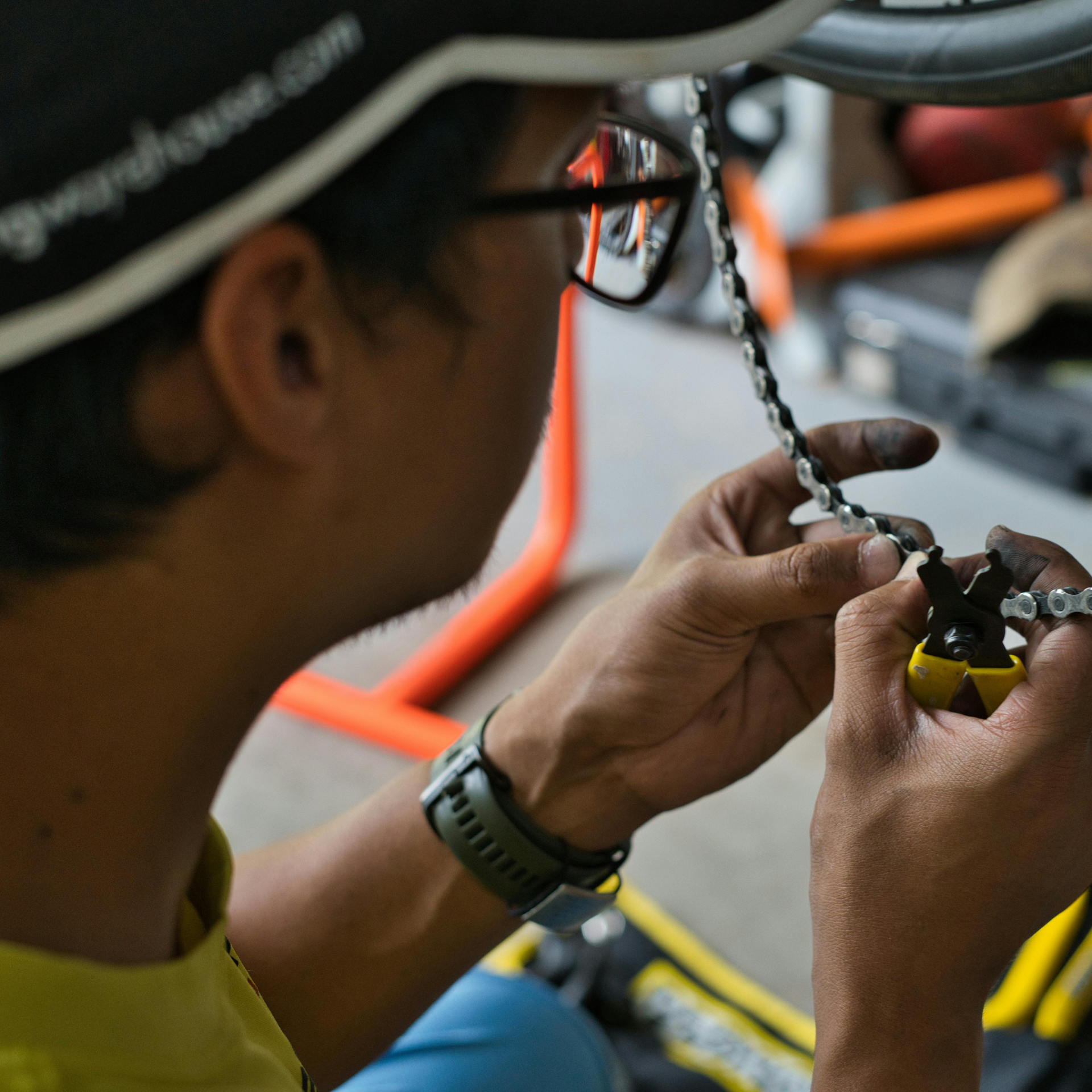 Person with glasses fixing a bike chain with tool in their hands.
