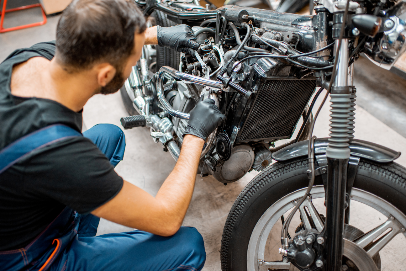 Mechanic working on a motorcycle engine. He wears gloves and overalls in a garage.