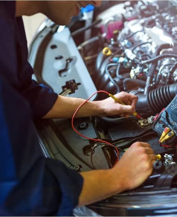 Mechanic working on car engine, using diagnostic tools. Inside a garage.