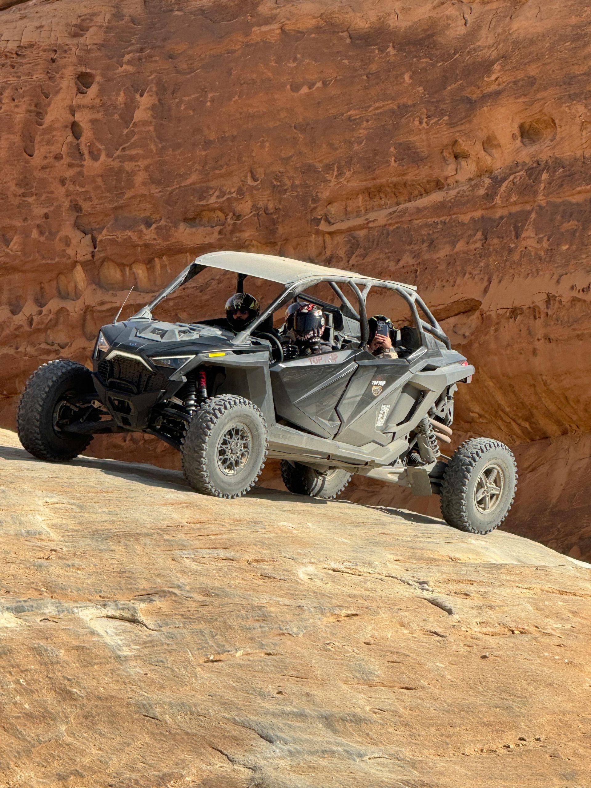 Black off-road vehicle driving on a rock surface in a desert landscape.