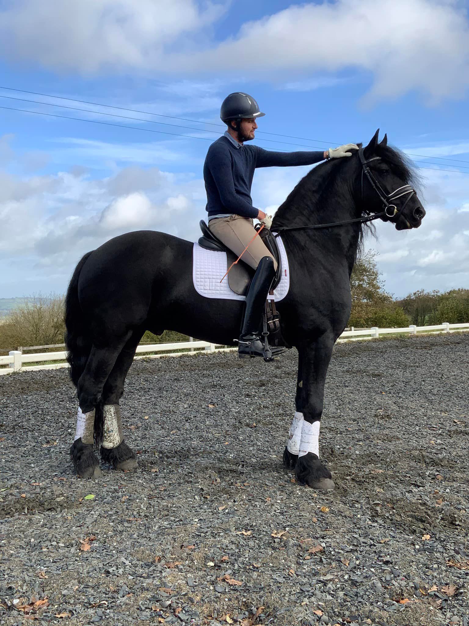 A man is riding a black horse on a gravel road.