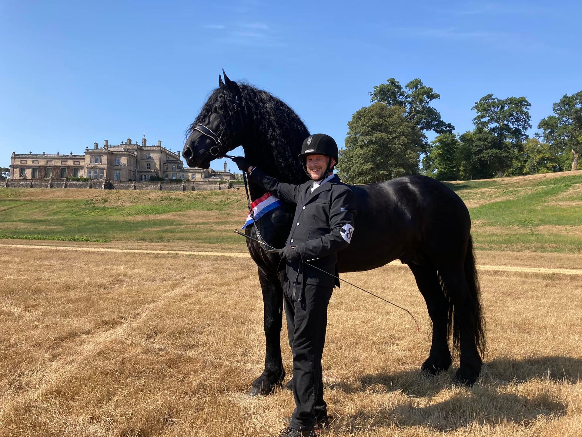 A man is standing next to a black horse in a field.