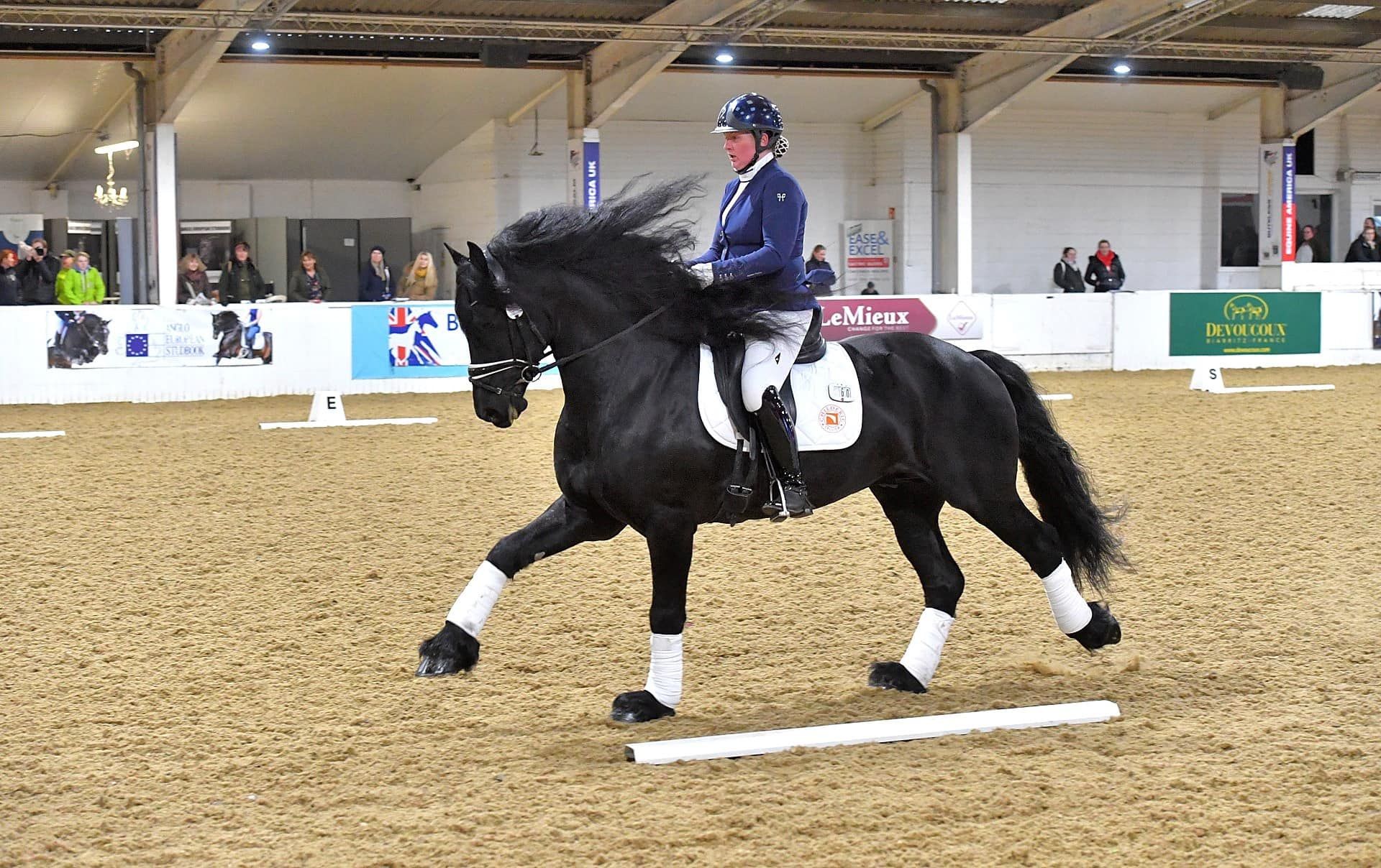 A man is riding a black horse on a dirt track.