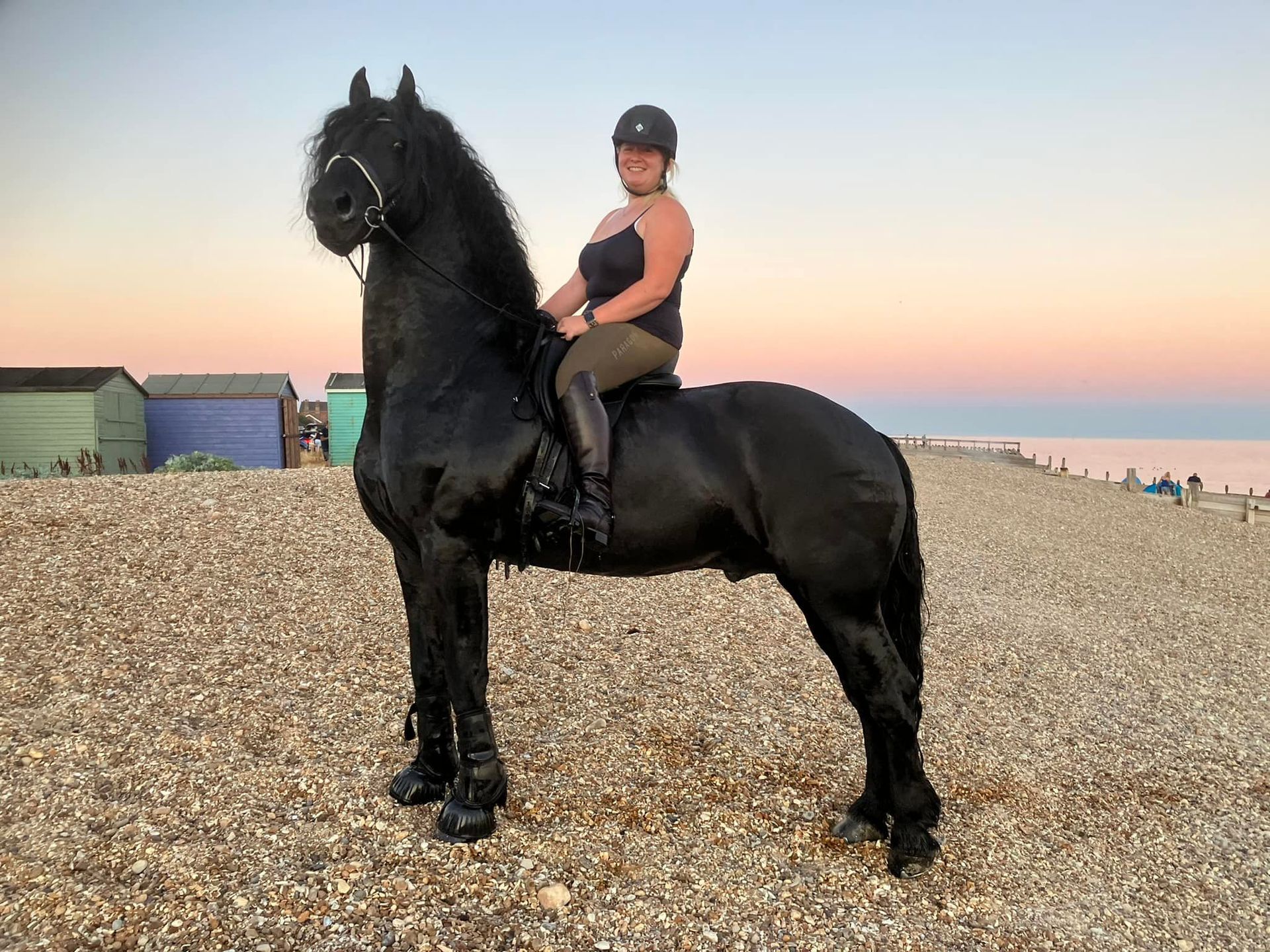 A woman is riding a black horse on a beach.