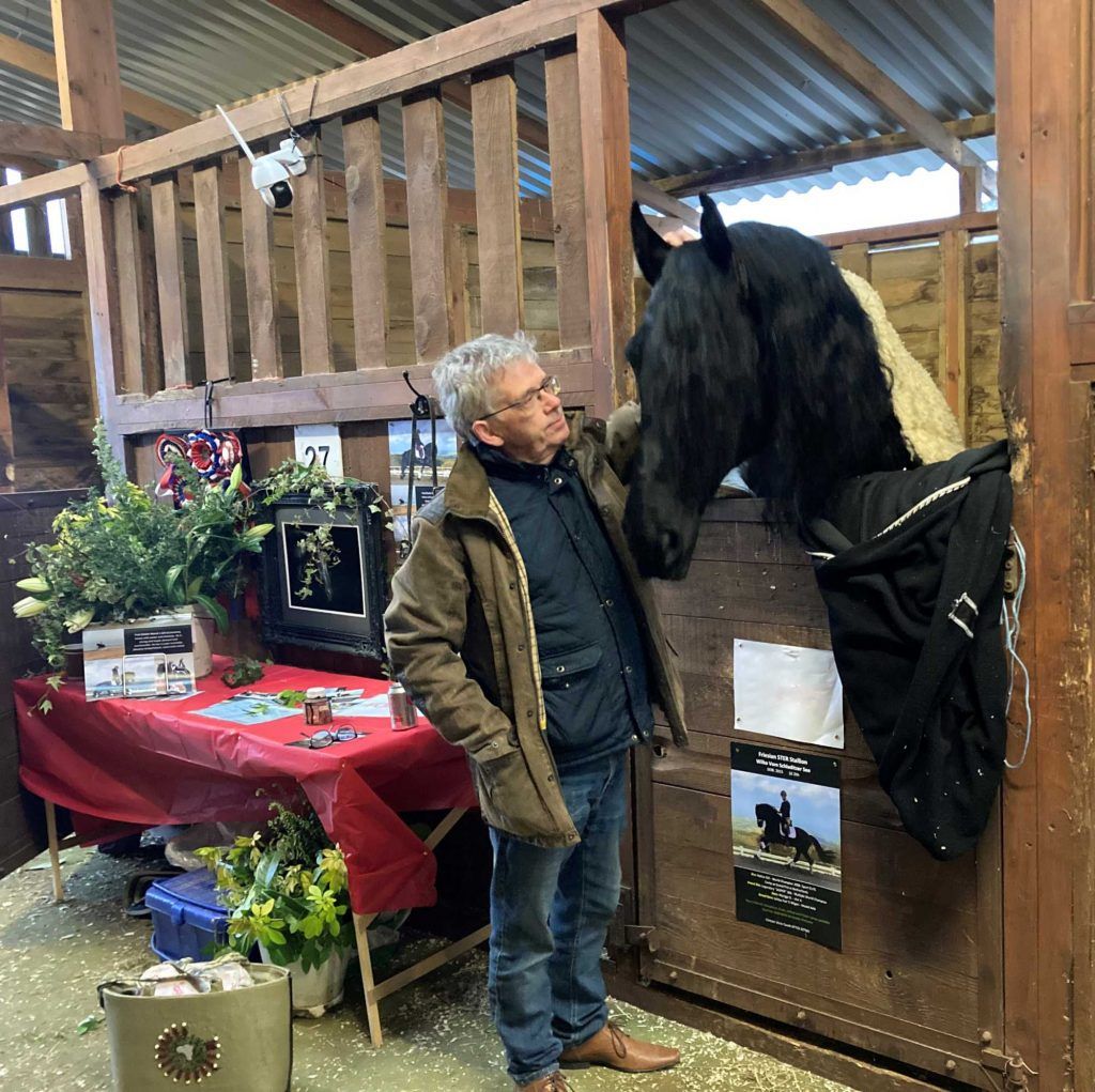 A man standing next to a black horse in a stable